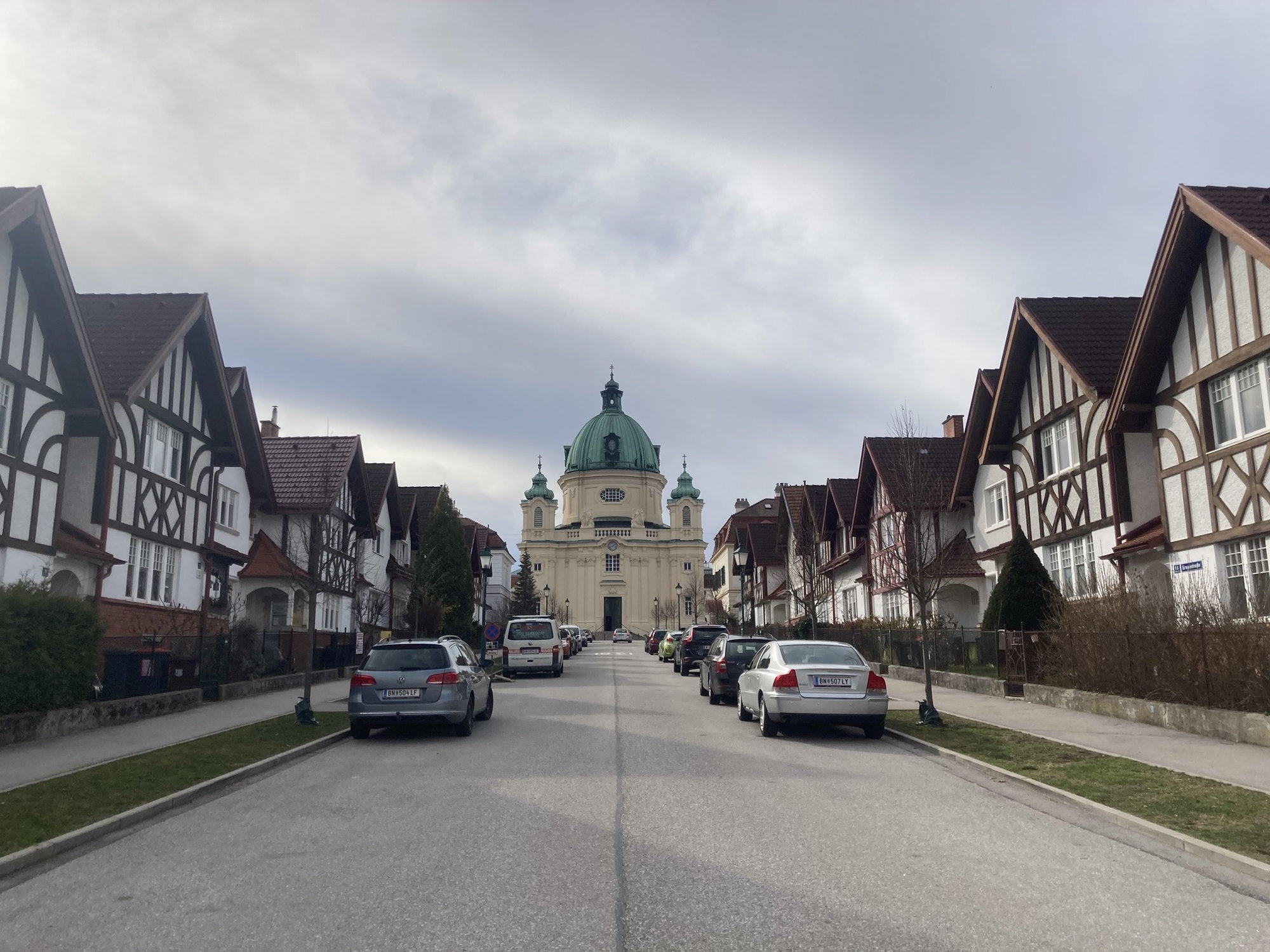 mittig im Hintergrund Kirche in Berndorf, links und rechts der Straße stehen Häuser mit Fachwerkoptik, vor den Häusern parken Autos