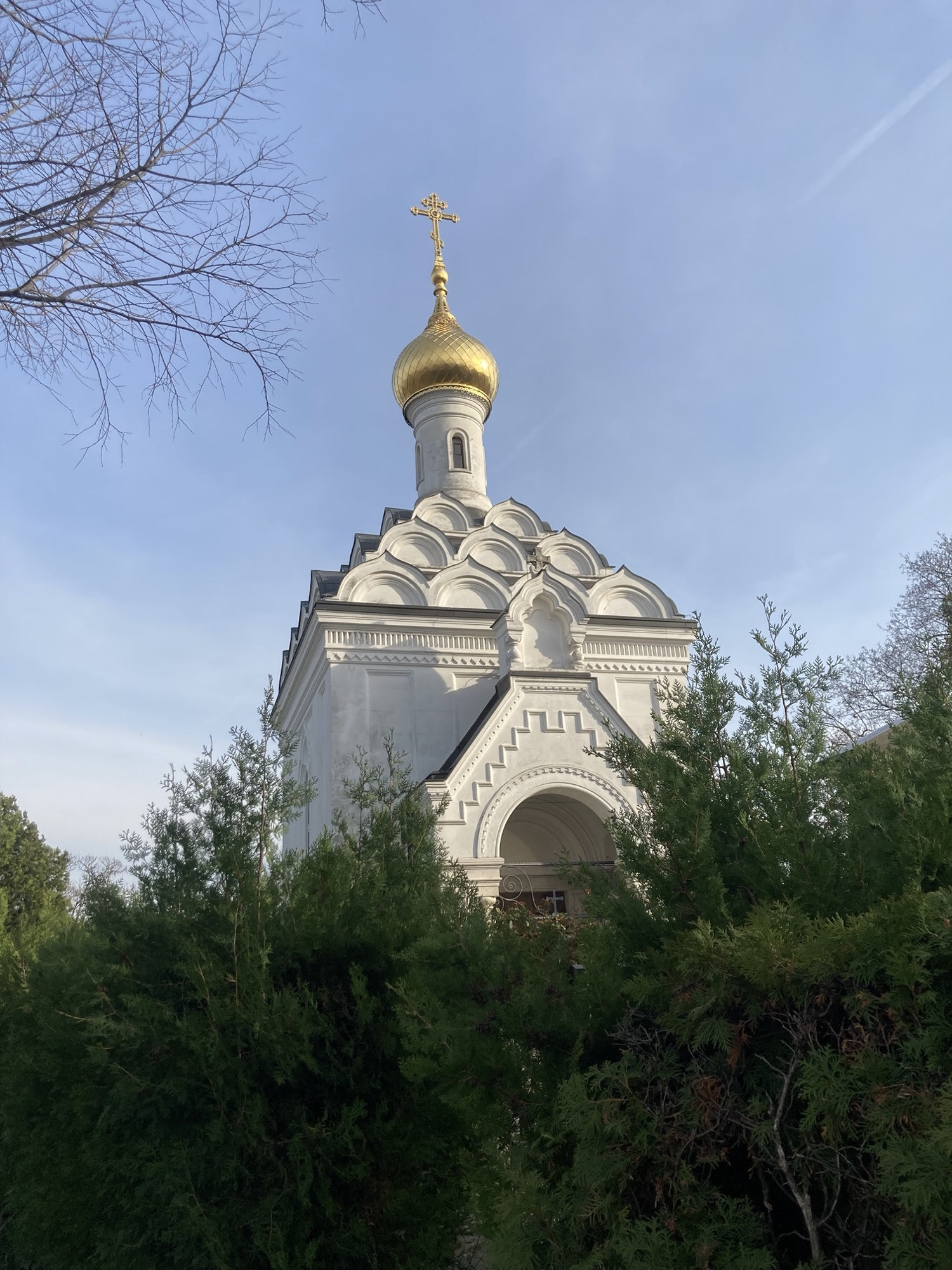 russisch-orthodoxe Lazarus-Kapelle, ein weißes Gebäude, das Dach besteht aus einer Art Schuppen und wird von einem einzelnen Turm mit einer goldenen Kuppel und dem orthodoxen Kreuz mit den zwei Querbalken gekrönt