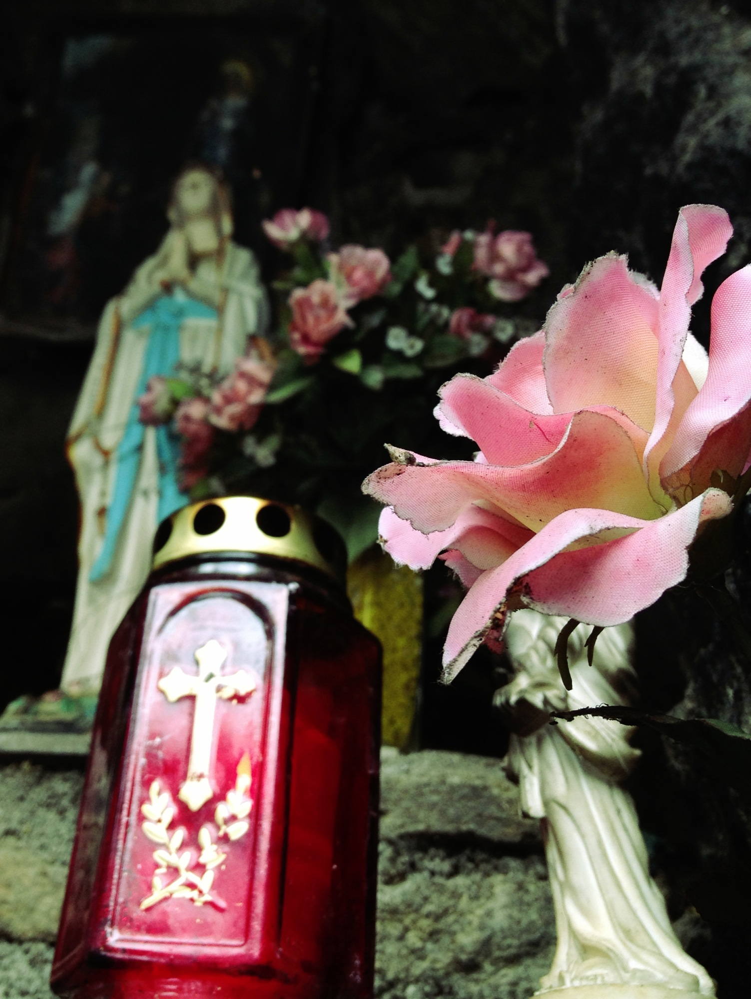 Kerzen, Stoffblumen und Marienfigur an der heiligen Quelle