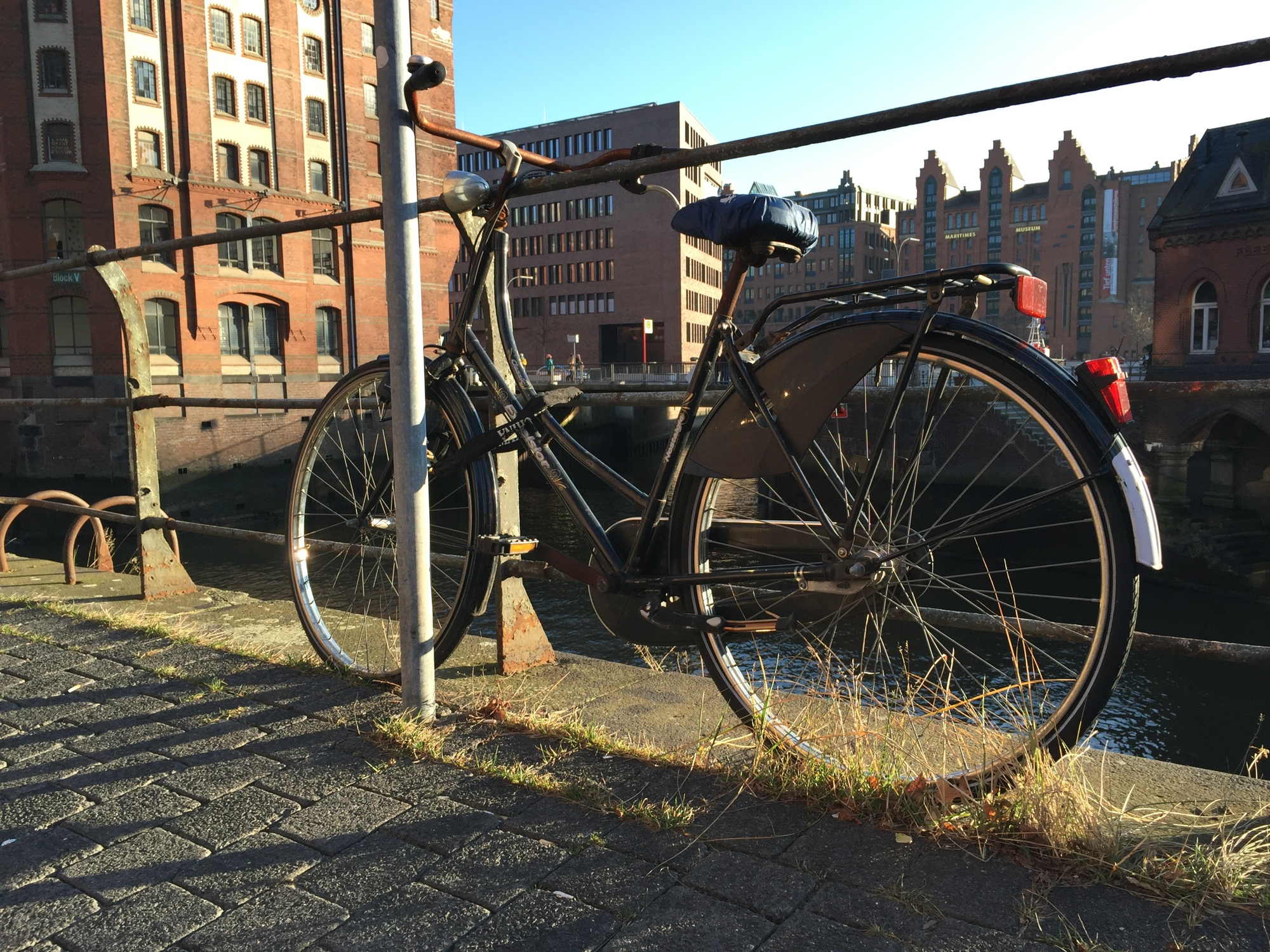 Hamburger Speicherstadt, ein Fahrrad ist an ein Geländer gekettet und wirft einen harten, schrägen Schatten auf das Pflaster