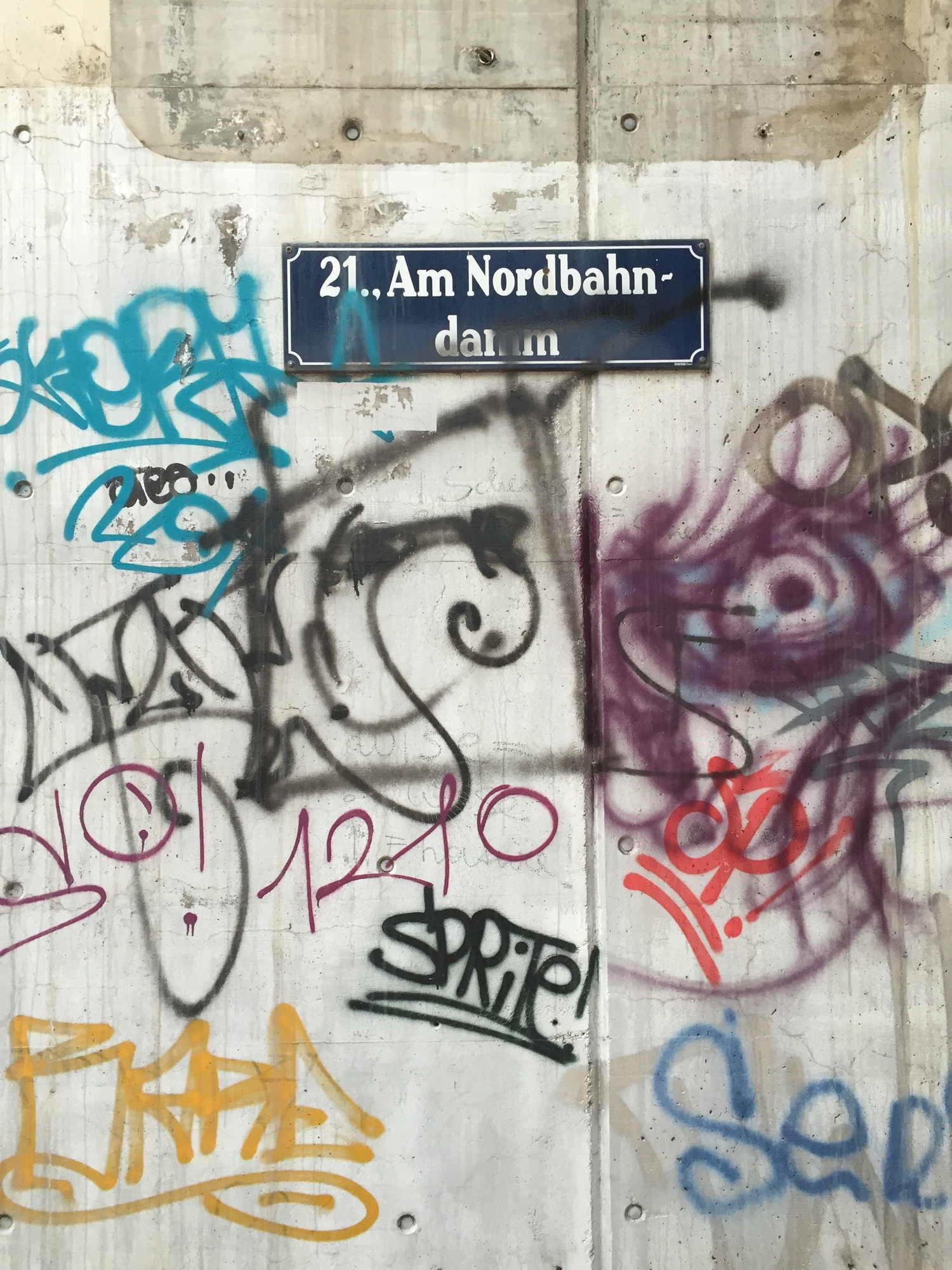 ein Schild „Am Nordbahndamm” neben der aufgelassenen Schnellbahnstation Strandbäder inklusive Graffiti