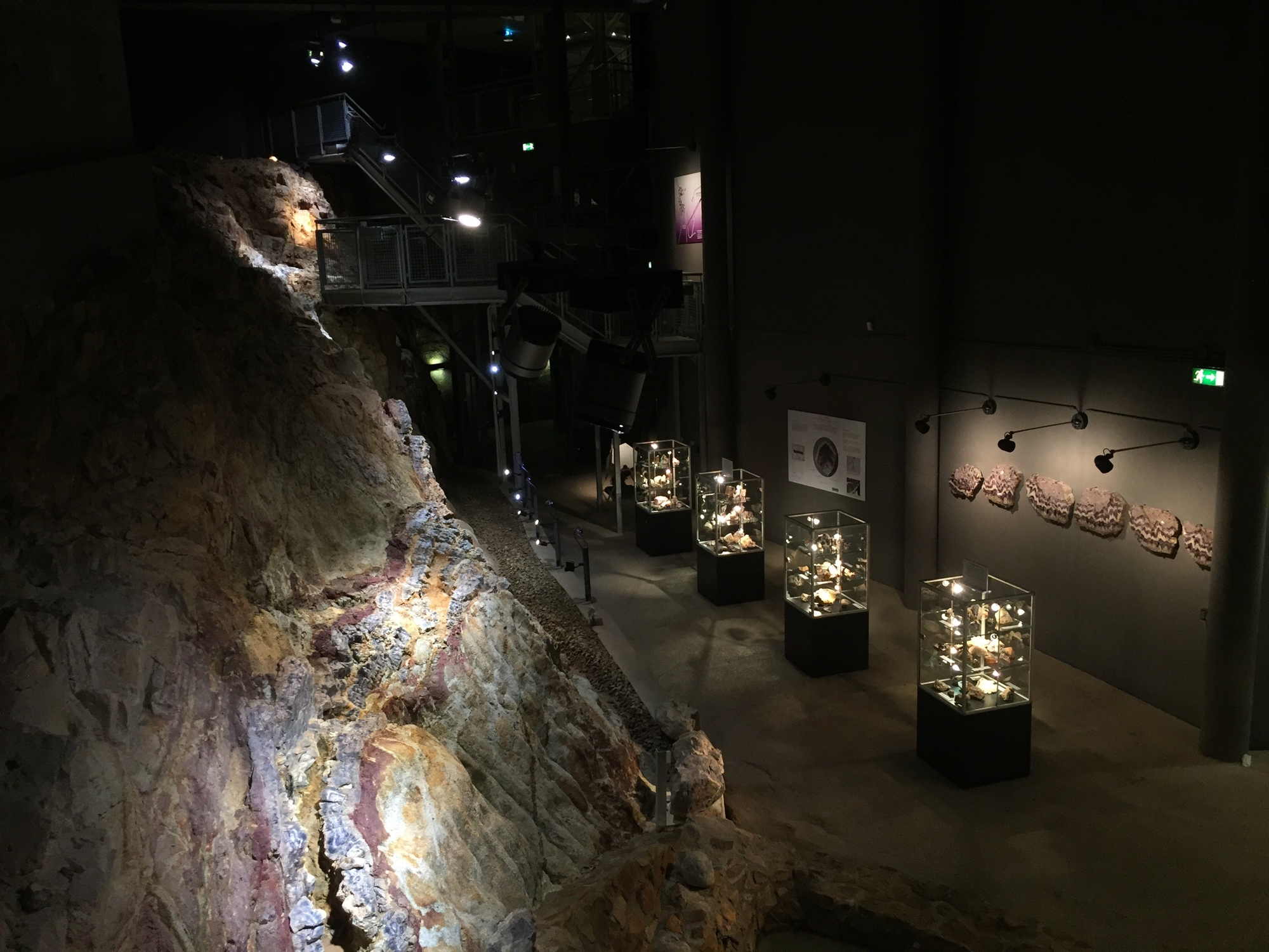 Blick in den Schaustollen, links ein Ausschnitt des Bänderamethystgangs, im Hintergrund Glasvitrinen mit verschiedenen verwandten Steinen, rechts an der Wand sechs Amethyst-Querschnitte