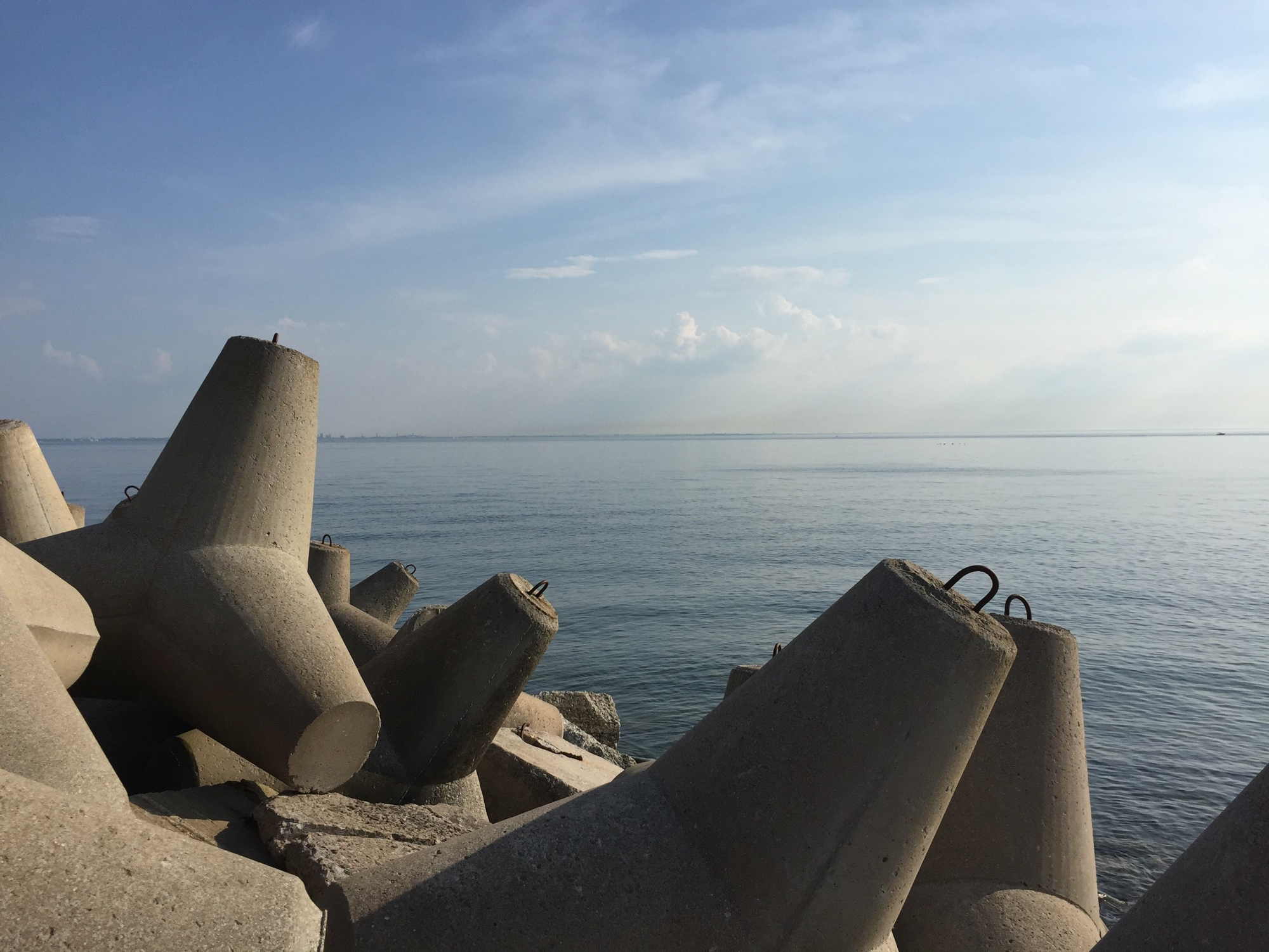 Betonpfeiler im Hafen von Aegna, die das Pier vor Wellen schützen, im Hintergrund ruhiges Meer mit einer Ahnung der sinkenden Sonne