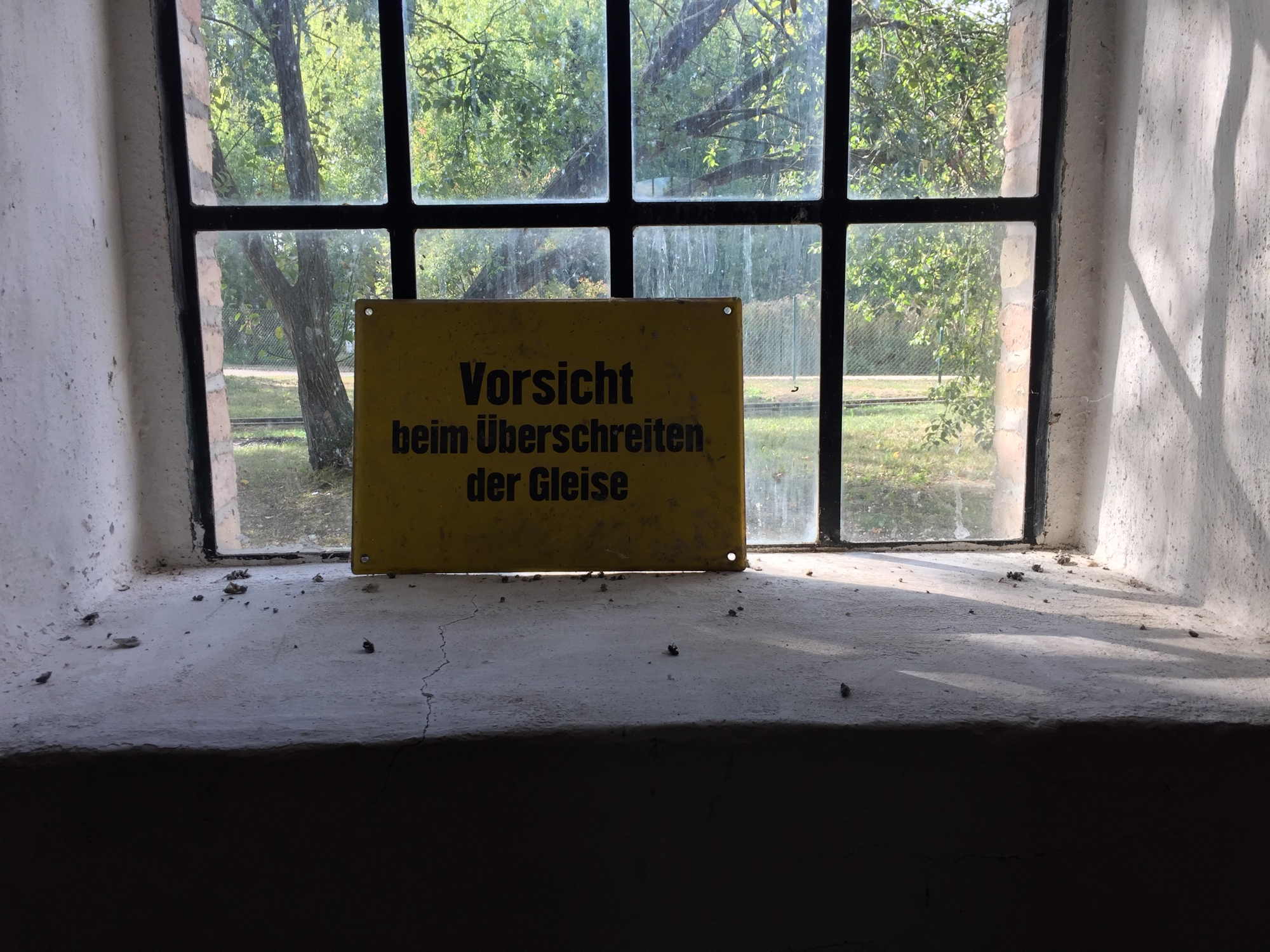 gelbes Schild „Vorsicht beim Überschreiten der Gleise“ vor einem Fenster