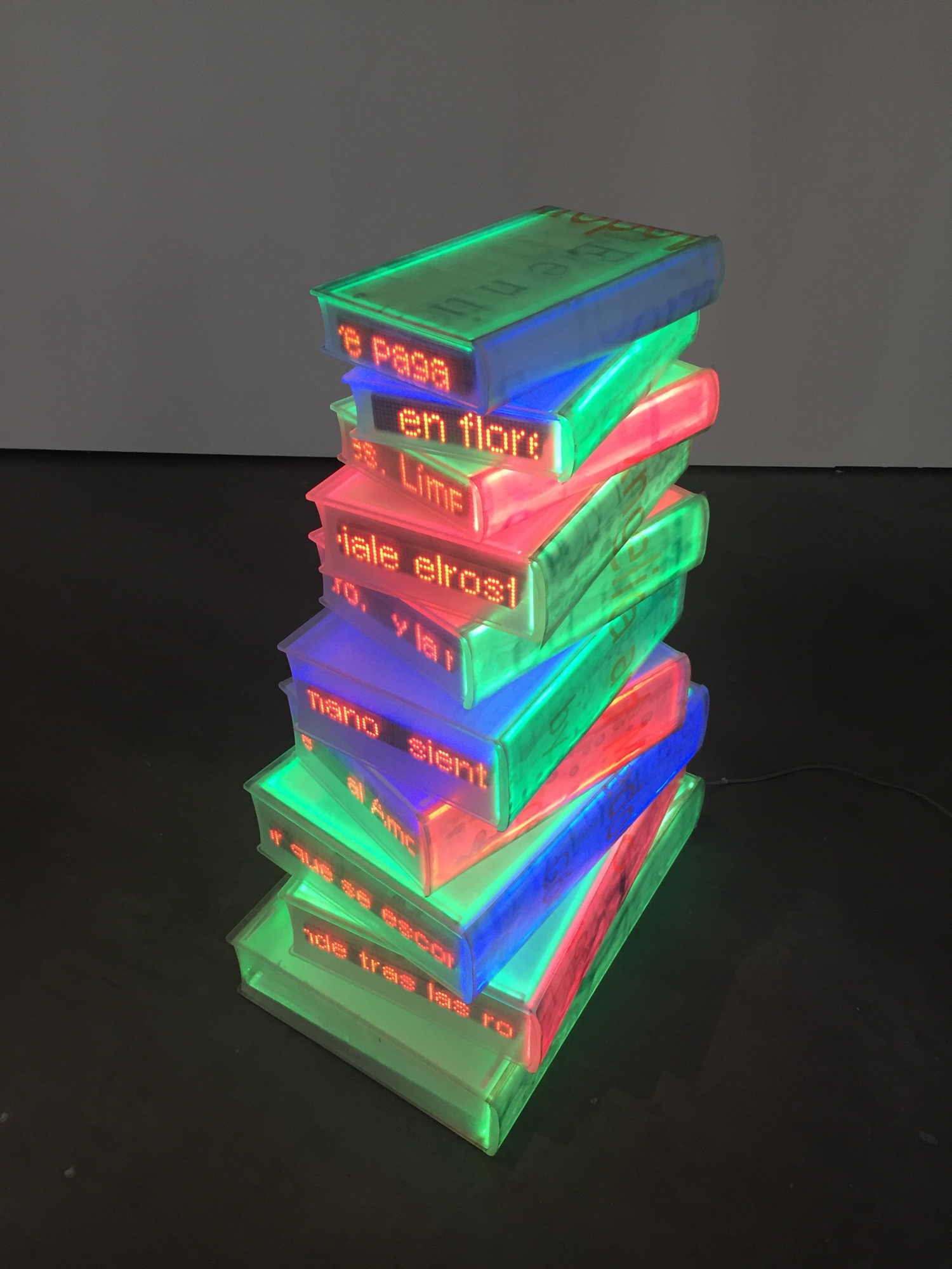 Skulptur aus buchförmigen transparenten Kästen, die bunt beleuchtet sind und an den Kanten mit Laufschrift Inhalte von Büchern darstellen