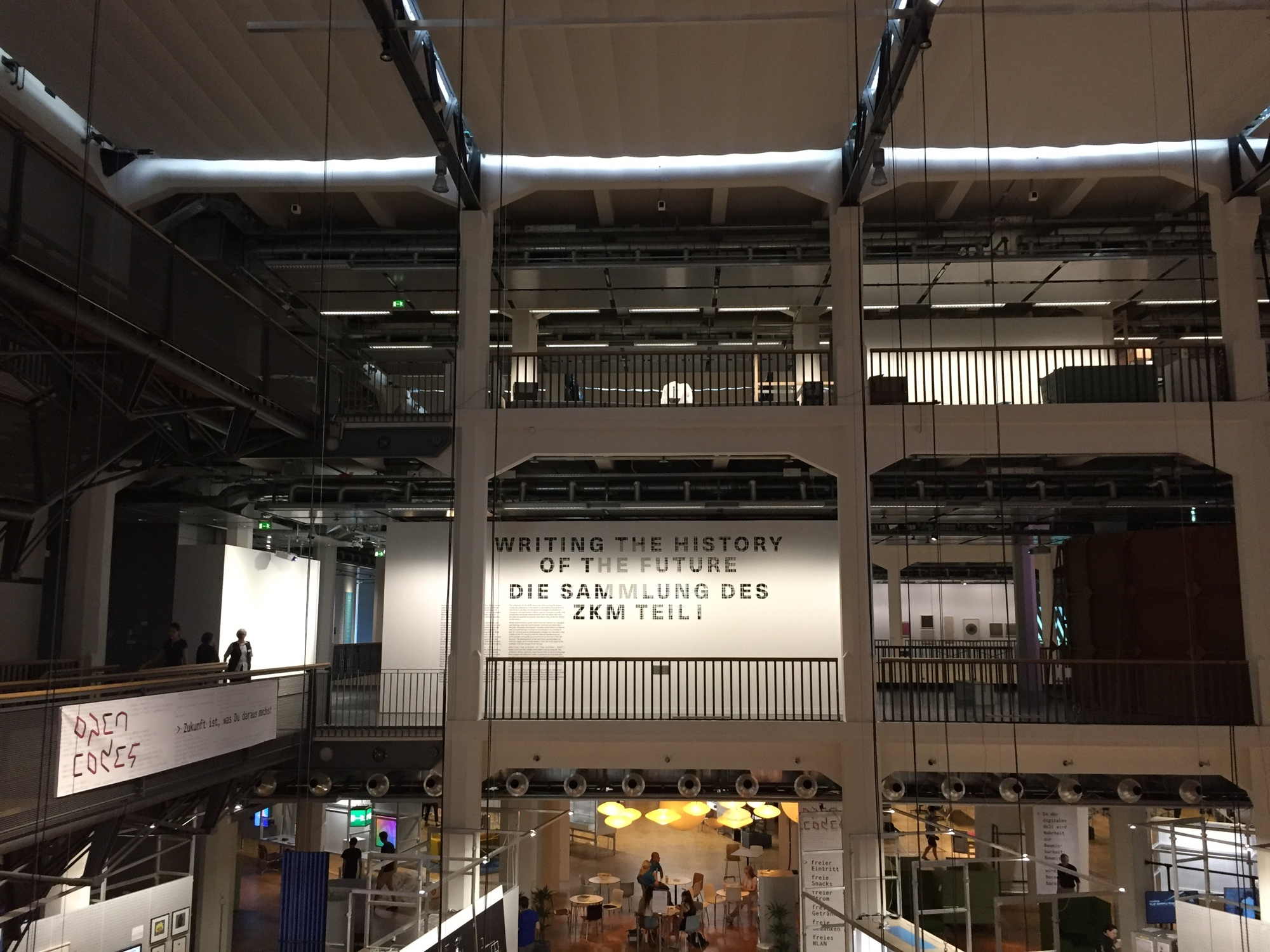 Blick über einen Lichthof des ZKM auf das Plakat einer aktuellen Ausstellung: Writing the history of the future: Die Sammlung des ZKM Teil 1