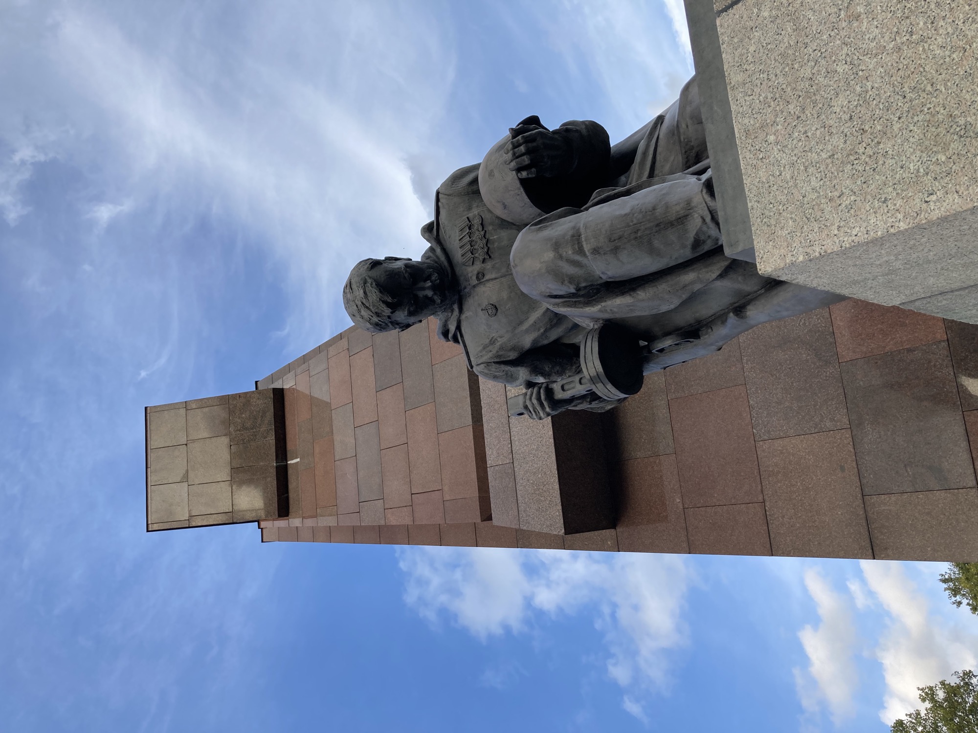 Sowjetisches Ehrenmal: Statue eines demütigen, knienden Soldaten mit Helm in der linken Hand und Maschinenpistole in der rechten Hand, dramatischer Blickwinkel von unten