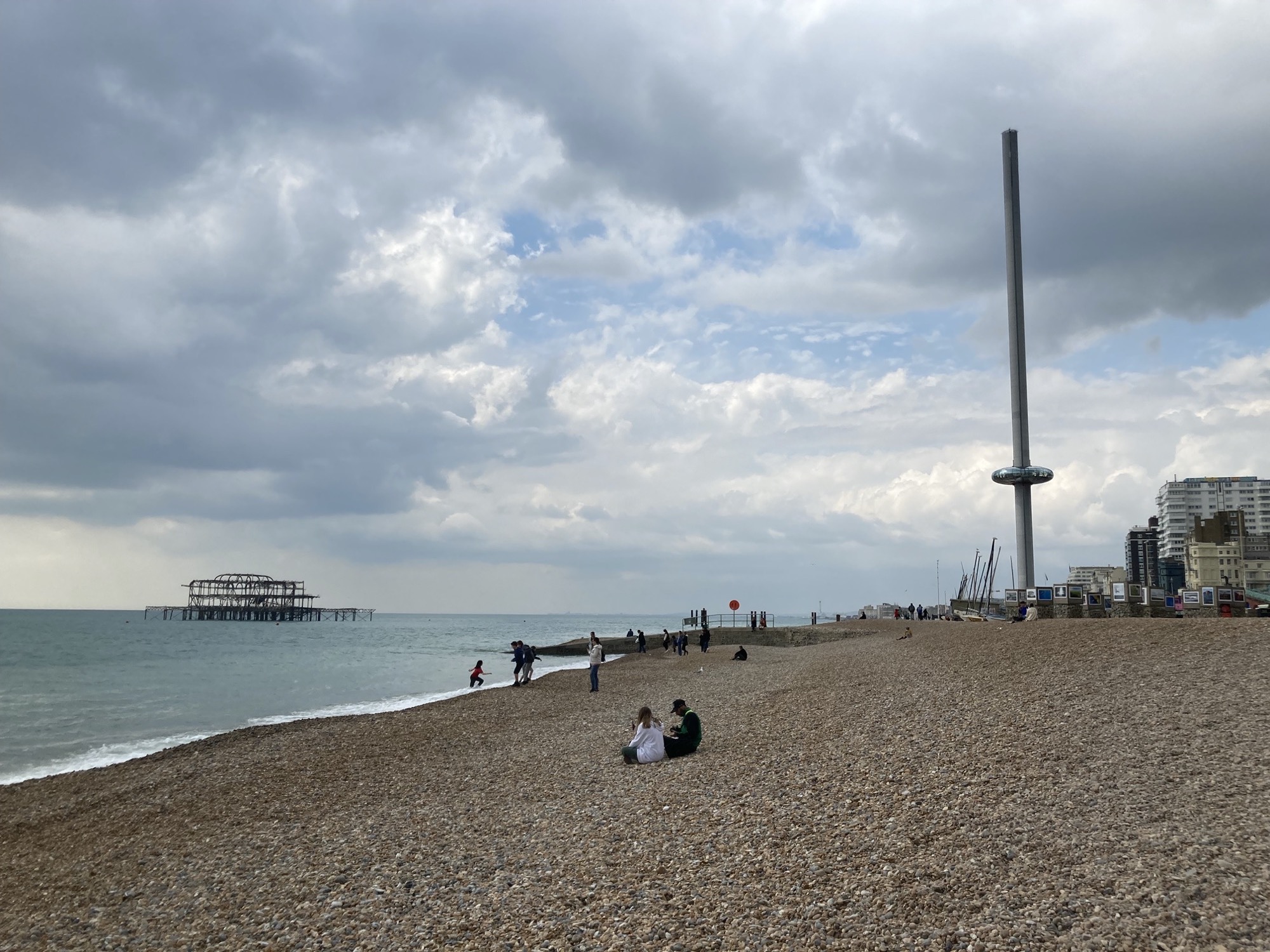 Strand in Brighton, links das Gerippe des abgebrannten West Piers, rechts im Hintergrund ein futuristischer Turm mit einer Art Donut drumherum, der i360 Tower