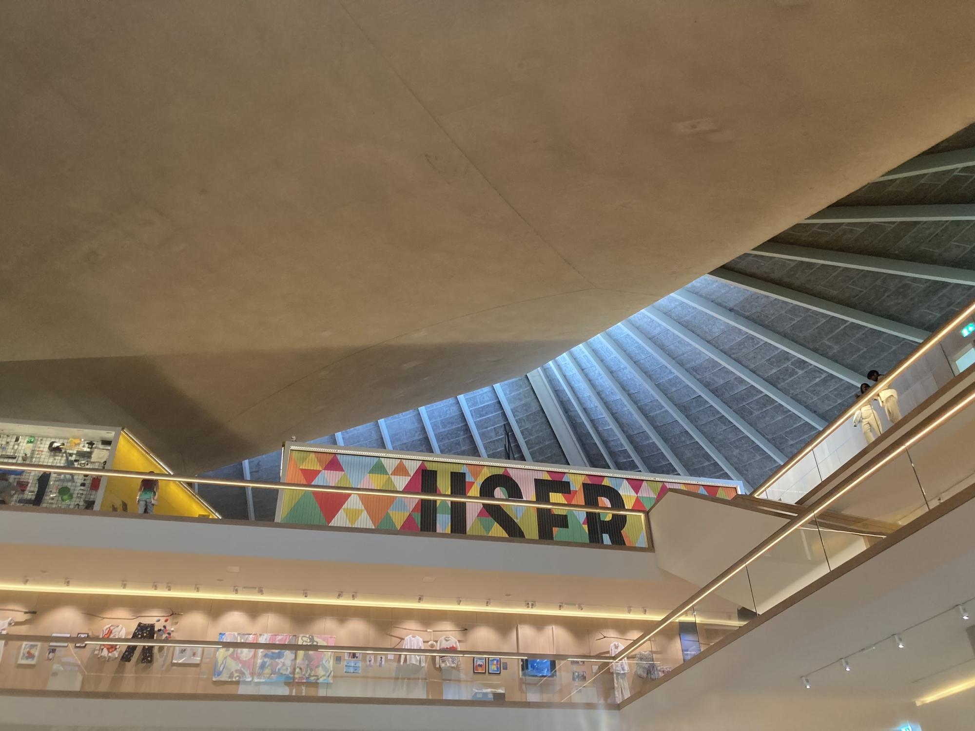 Blick von unten schräg Richtung Dach des Design Museums, rechts oben eine Textwand mit dem Schriftzug User, im Stockwerk darunter ist Kleidung aus der Modeausstellung zu sehen