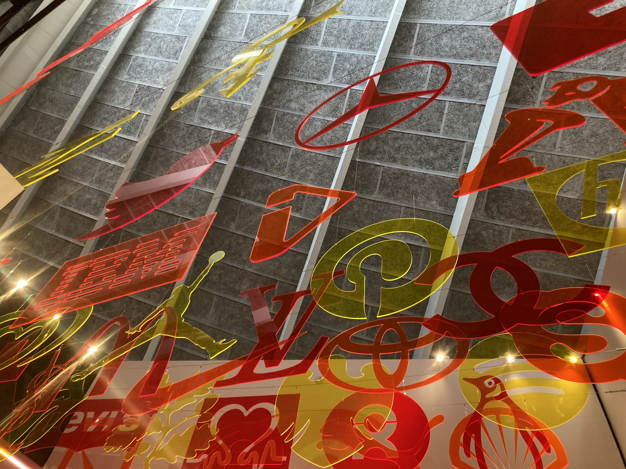 von der Decke hängen aus Plexiglasplatten (in den Farben gelb, rot, orange) ausgeschnittene Logos zB Twitter, Mercedes, Skype, IBM