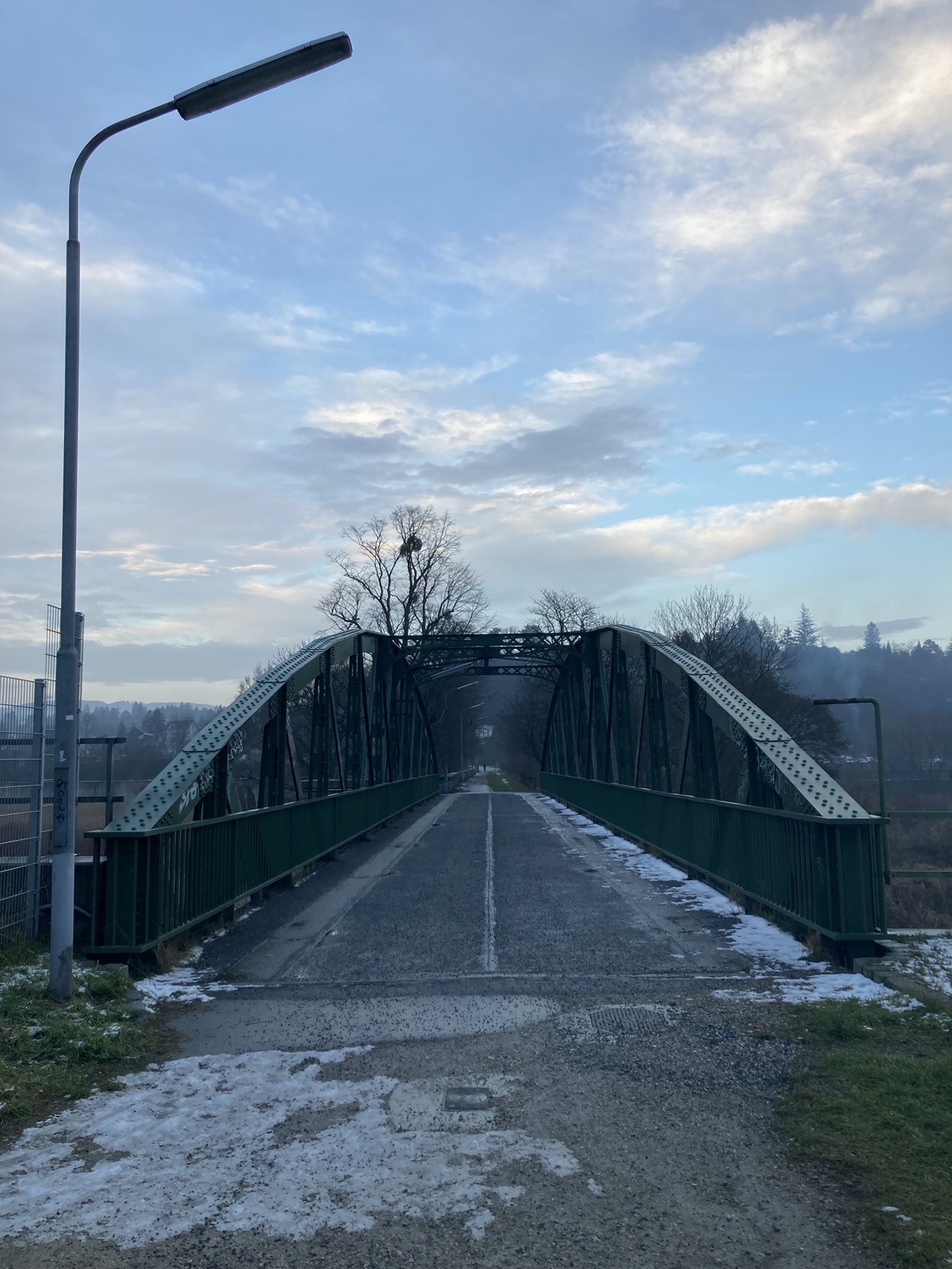Brücke über den Wienfluss, grüne Metallkonstruktion an den Seiten, leicht bewölkter Himmel, düstere Stimmung, einzelne Schneeflecken am Boden