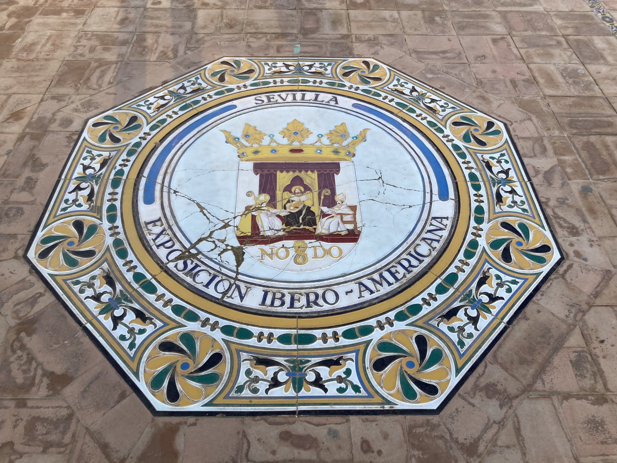 Detailaufnahme eines Mosaiks auf dem Boden, Form achteckig, in der Mitte das Stadtwappen von Sevilla mit dem Schriftzug NO DO, darunter der Text Exposicion Ibero-Americana, das Mosaik ist leicht beschädigt und von einigen Sprüngen durchzogen