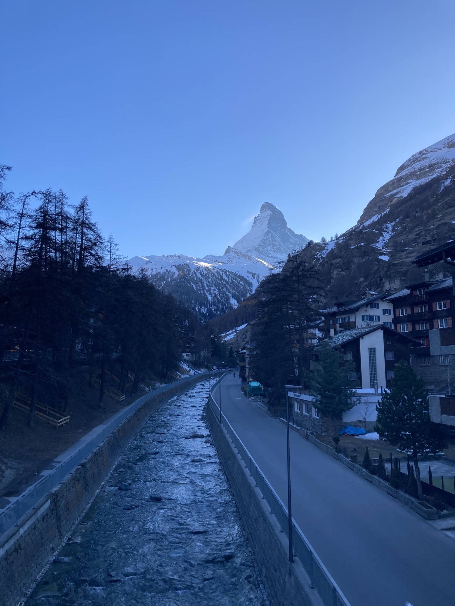 der berühmte Berg Matterhorn, noch von der Sonne beleuchtet, im Vordergrund ein Fluss, der sich auf den Berg zuwindet, die Bildstimmung ist bläulich, wie in einem Tal, in das die Sonne gerade nicht mehr hinein scheint, aber es ist noch hell