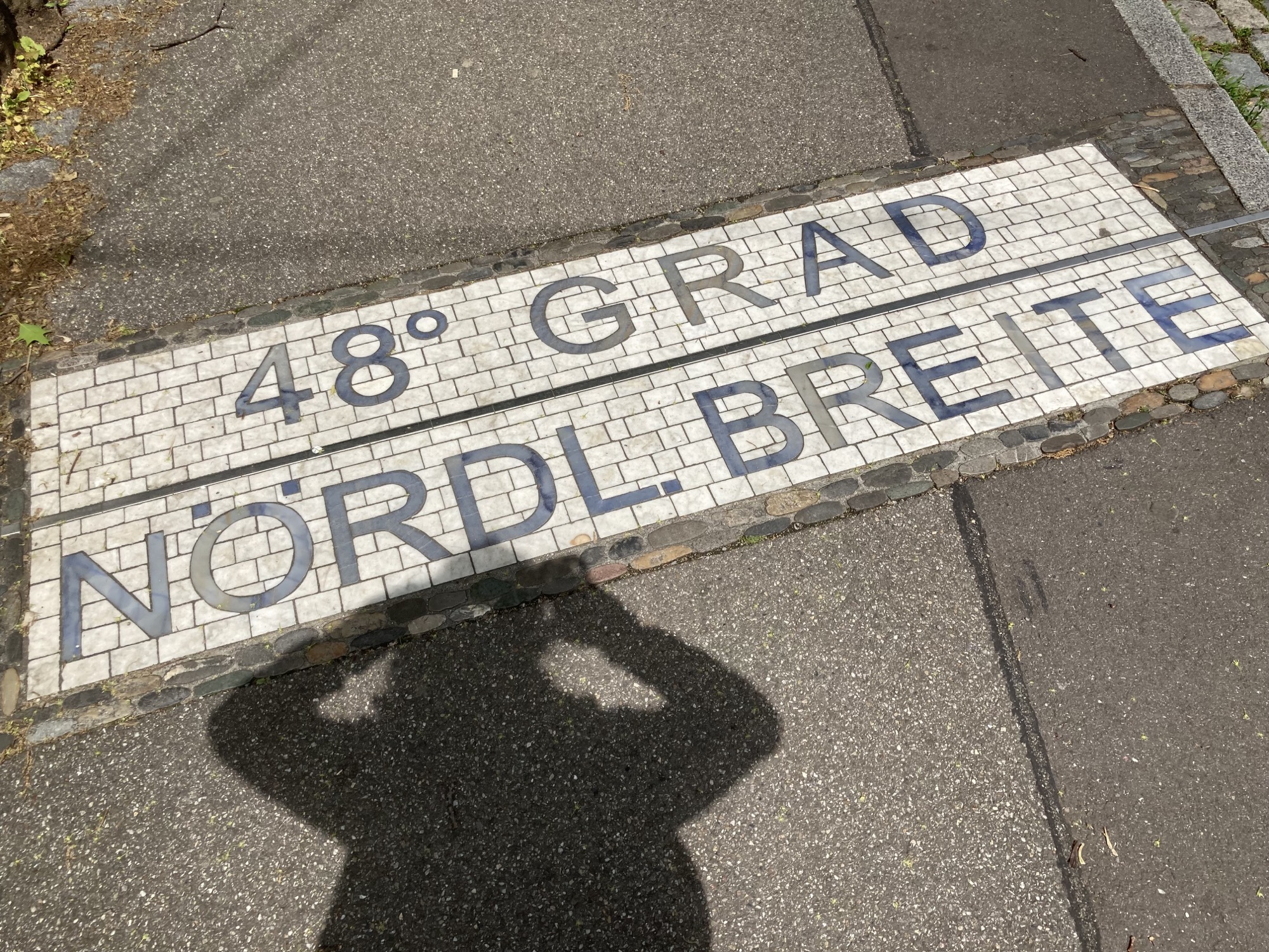 der 48. Breitengrad in Freiburg, Markierung auf dem Boden mit der Beschriftung „48° Grad Nördl. Breite“, der Schatten der Fotografin ist neben dem Schriftzug zu sehen