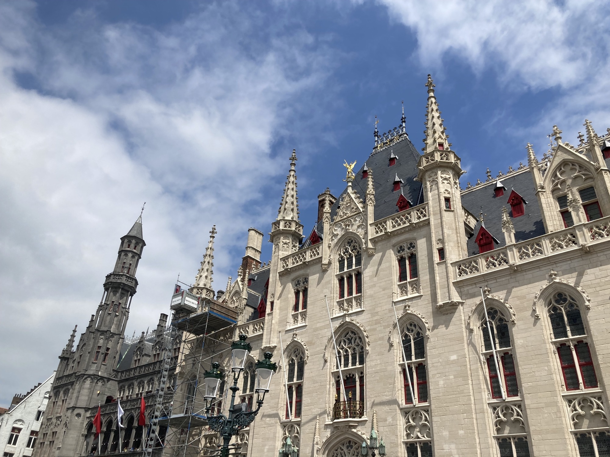 spätgotische Architektur des Rathaus von Brügge, weiße Ziegel, dekorative Türmchen und besonders auffällige kleine rote Giebel, die zwischen den grauen Dachschindeln hervorragen