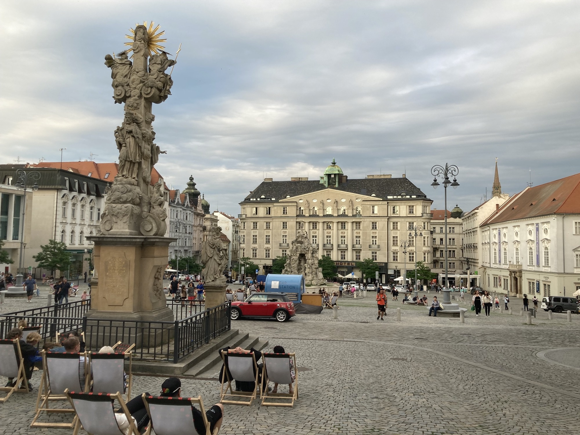 zentraler Marktplatz in Brno, im Vordergrund Liegestühle vor einer Pestsäule, dahinter ein weiter Platz, der von einem altmodischen Hotel begrenzt wird