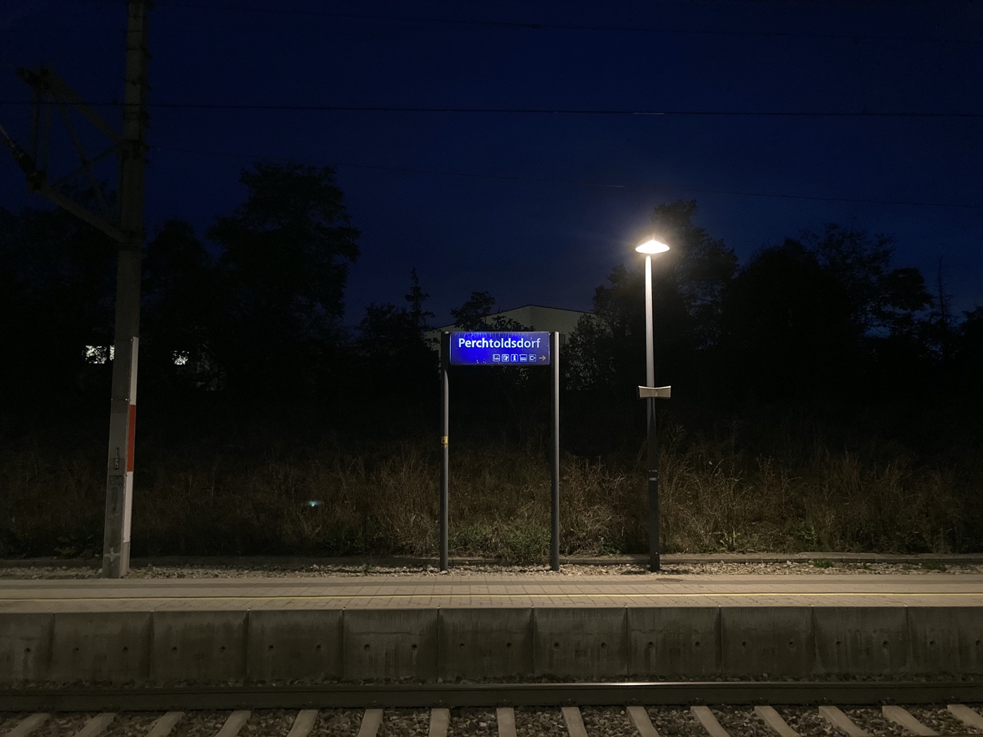 Abend am Bahnhof Perchtoldsdorf, Schild auf dem Bahnsteig beleuchtet von einer einsamen Laterne