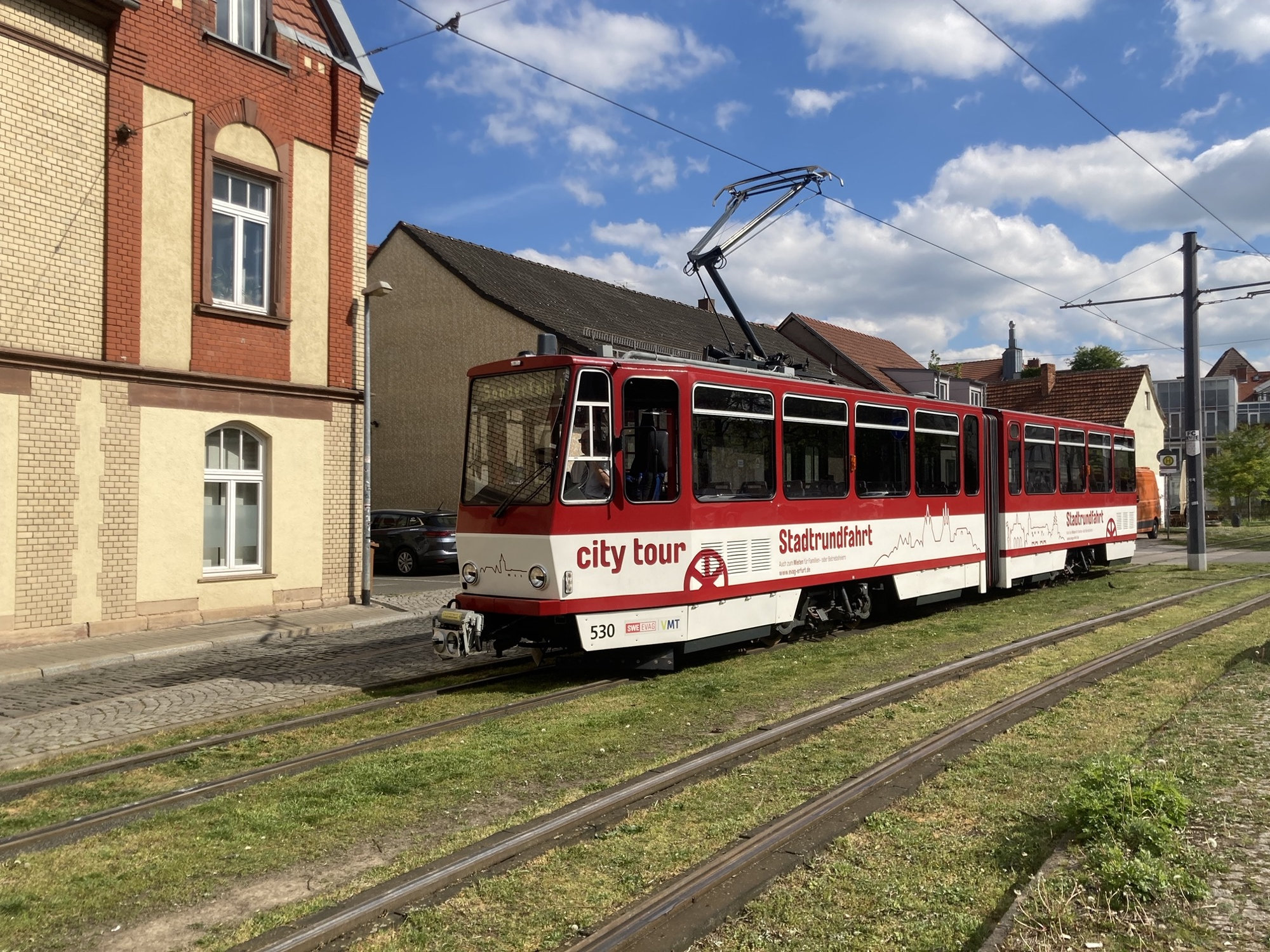 altmodische Straßenbahn mit der Aufschrift „city tour Stadtrundfahrt“, sie steht auf Rasengleis und wird gleich zu einer Sonderfahrt abfahren