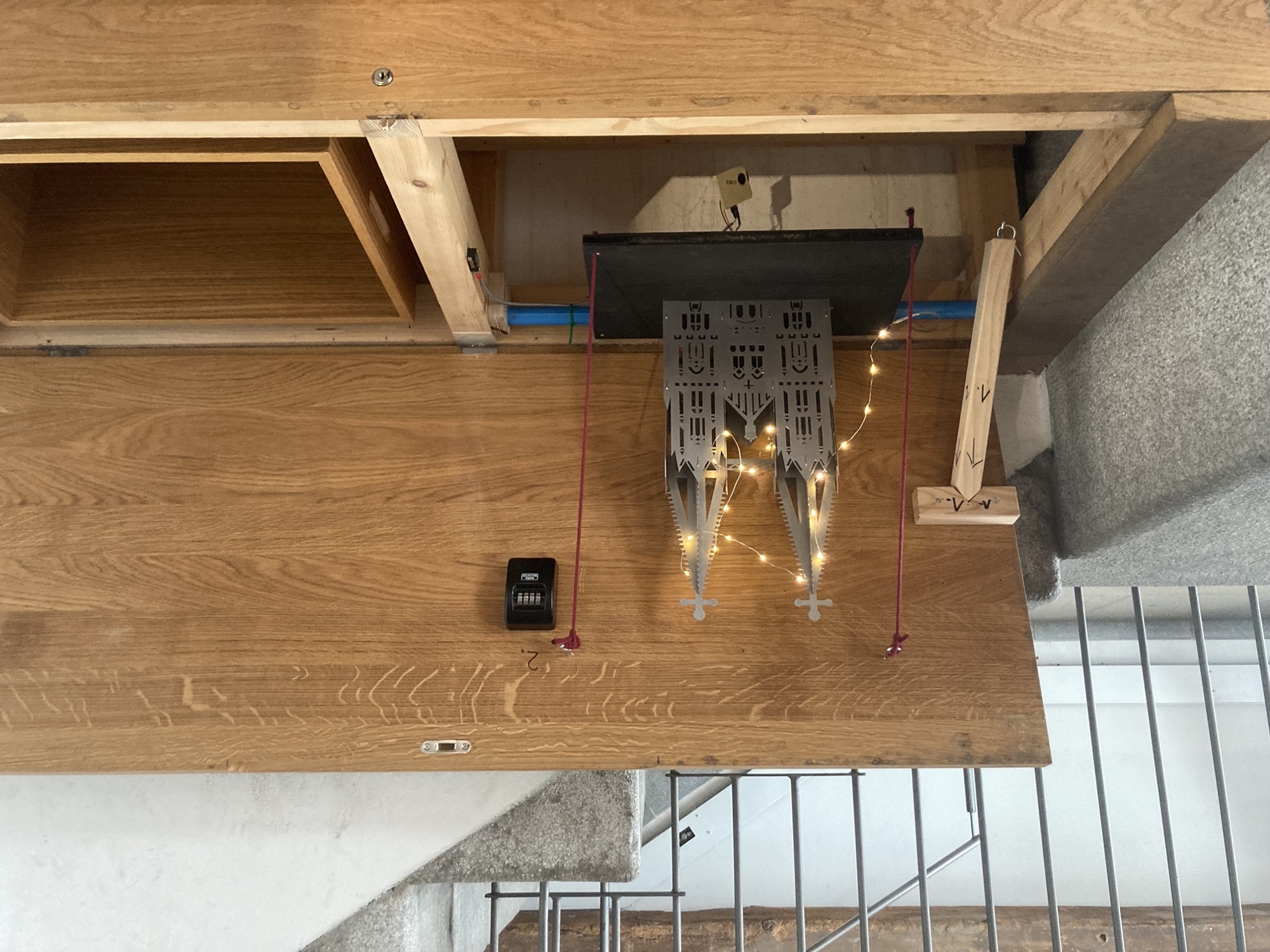 eine breite Holzbox mit offenem Deckel neben einer Treppe, ein Metallmodell des Regensburger Doms ist von einer kleinen LED-Lichterkette beleuchtet, daneben ein kleines Zahlenschloss