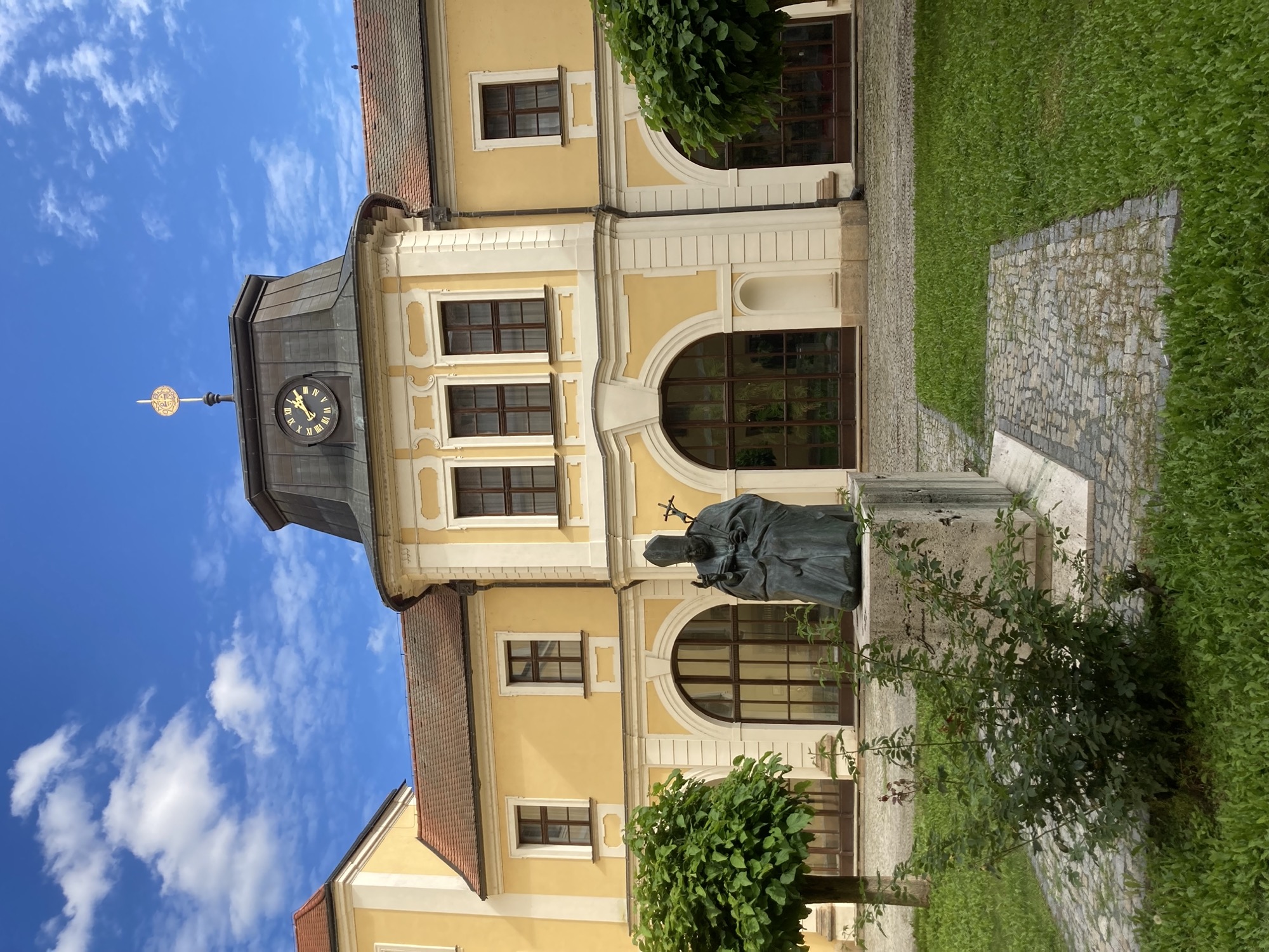 Innenhof eines Klosters, in der Mitte die Metallstatue eines Papstes mit Mitra und Kreuz, der mit der rechten Hand winkt