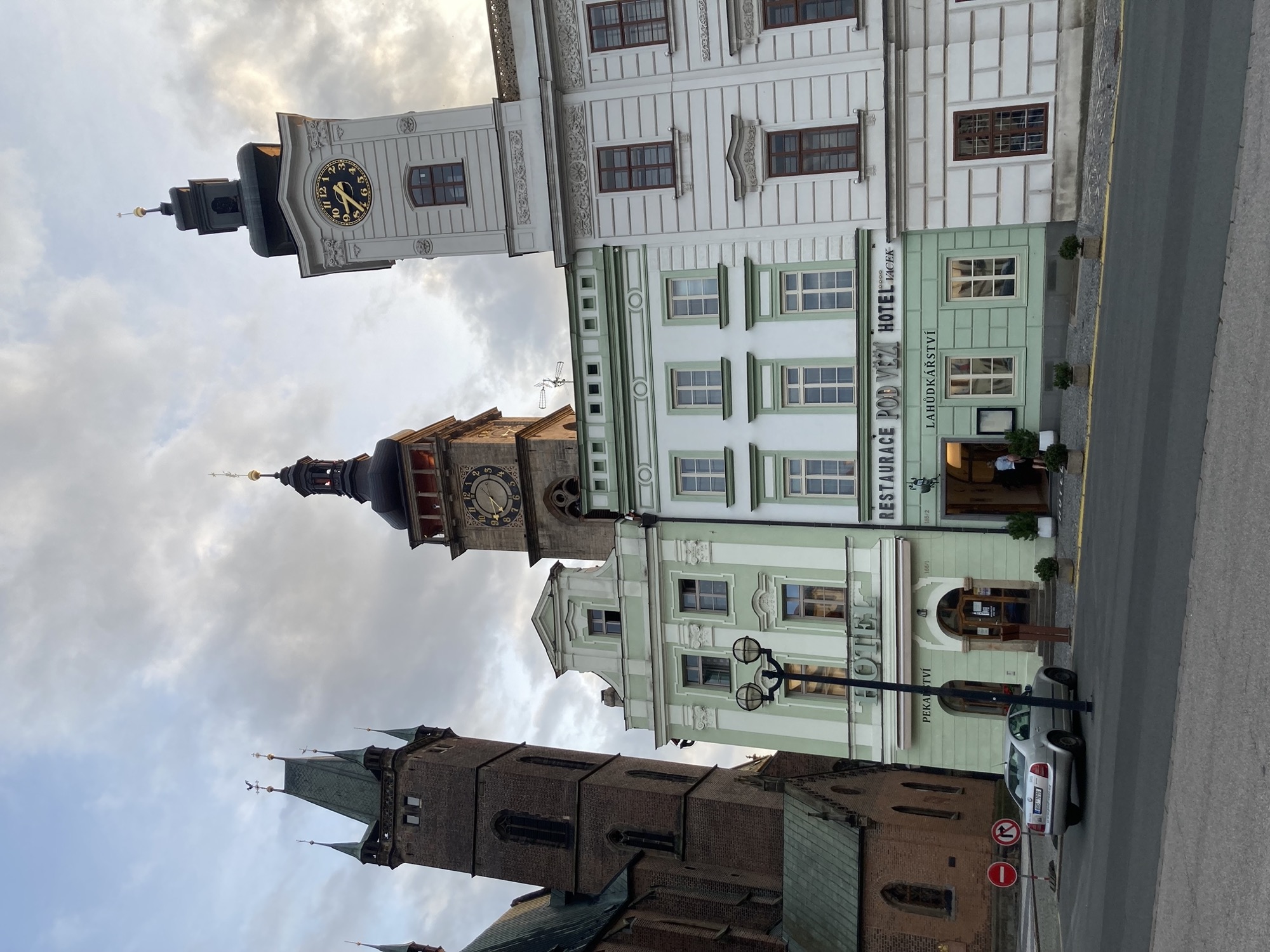 Häuserzeile mit drei Türmen, links der braune Turm einer Kirche, in der Mitte ein Turm mit einer Uhr und einem Balkon, rechts ein weißer Turm, der direkt auf dem Gebäude sitzt, die Häuser sind grün-weiß gestrichen und verziert