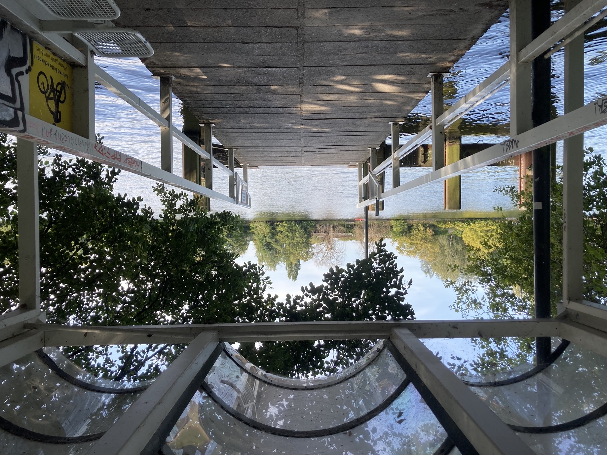 Anlegestelle der Fähre F11 am Baumschulenweg, links und rechts ist der Steg von einem weißen Geländer begrenzt, nach vorne hin zur Spree offen, darüber ragt oben ein dreiteiliges abgerundetes Dach ins Bild