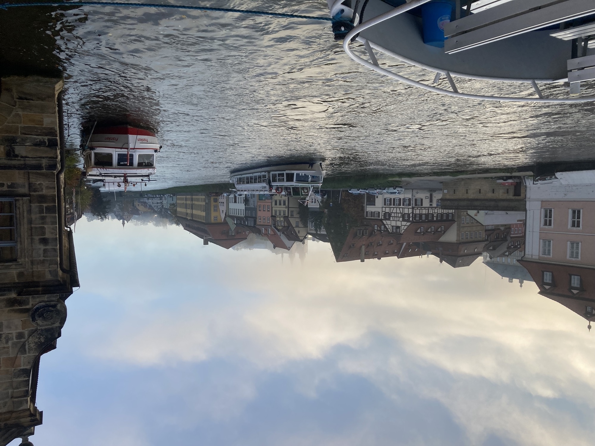 Blick übers Wasser des linken Regnitzarms, 2 Ausflugsschiffe sind zu sehen, am Flussufer altmodische Fachwerkhäuser, dahinter verschwinden die zwei Türme einer Kirche im Nebel, der sich gerade über der Stadt niedersenkt