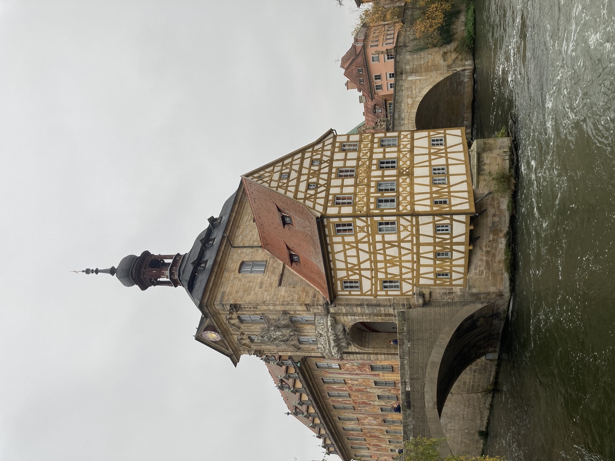 das Alte Rathaus thront auf einem Felsen inmitten des linken Regnitzarms, links und rechts führt die Obere Brücke durch das Gebäude, auf einer Spitze vorgelagert ist ein Teil des Rathauses, der aus hell gestrichenen Fachwerkbalken besteht