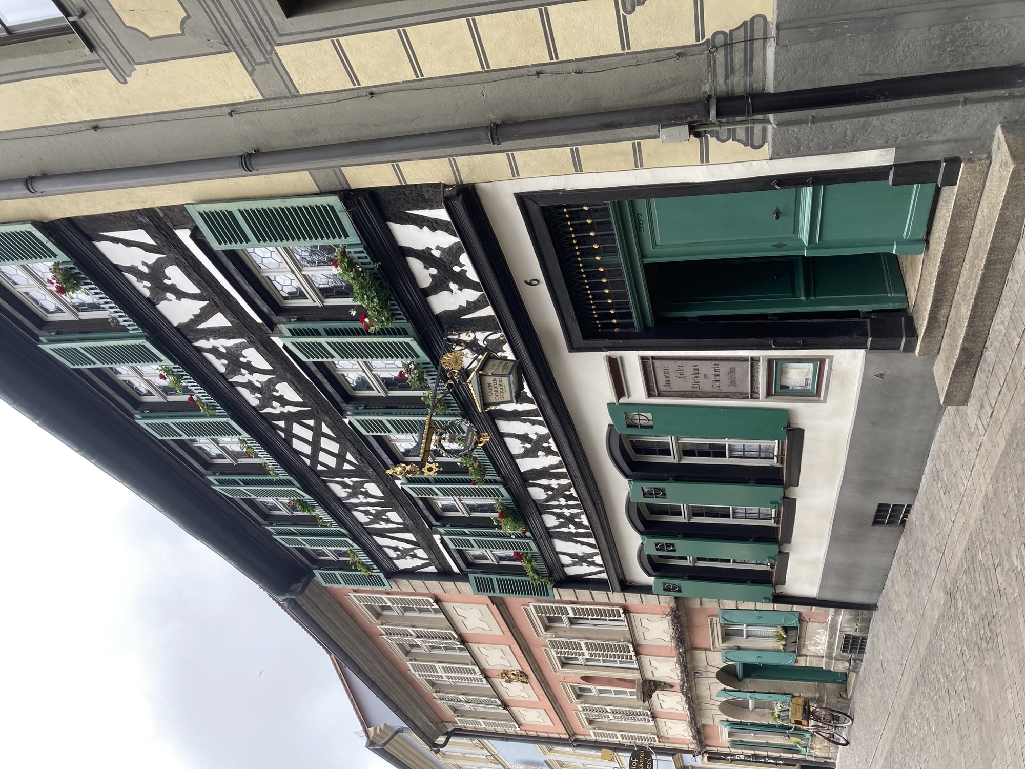 Gebäude der Traditionsbrauerei Schlenkerla, Fachwerkhaus mit grünen Fensterläden, über dem Eingang hängt eine Lampe mit viel Dekoration zB ein Lorbeerkranz, die Figur eines schlafenden Löwens und ein goldener Davidsstern (Symbol für eine Brauerei)