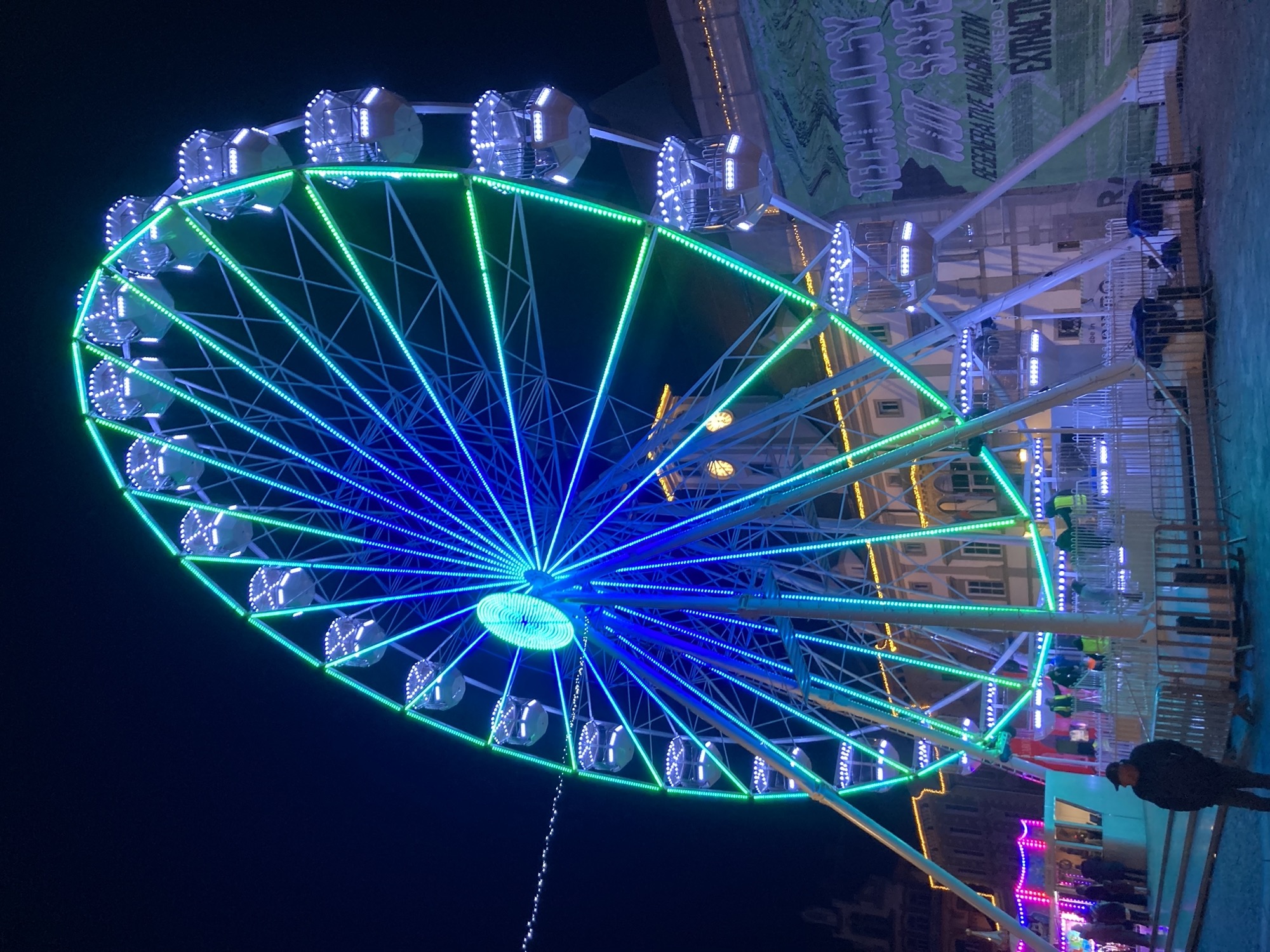 Nachtaufnahme, ein blau-grün beleuchtetes Riesenrad mit ca. 25 Gondeln