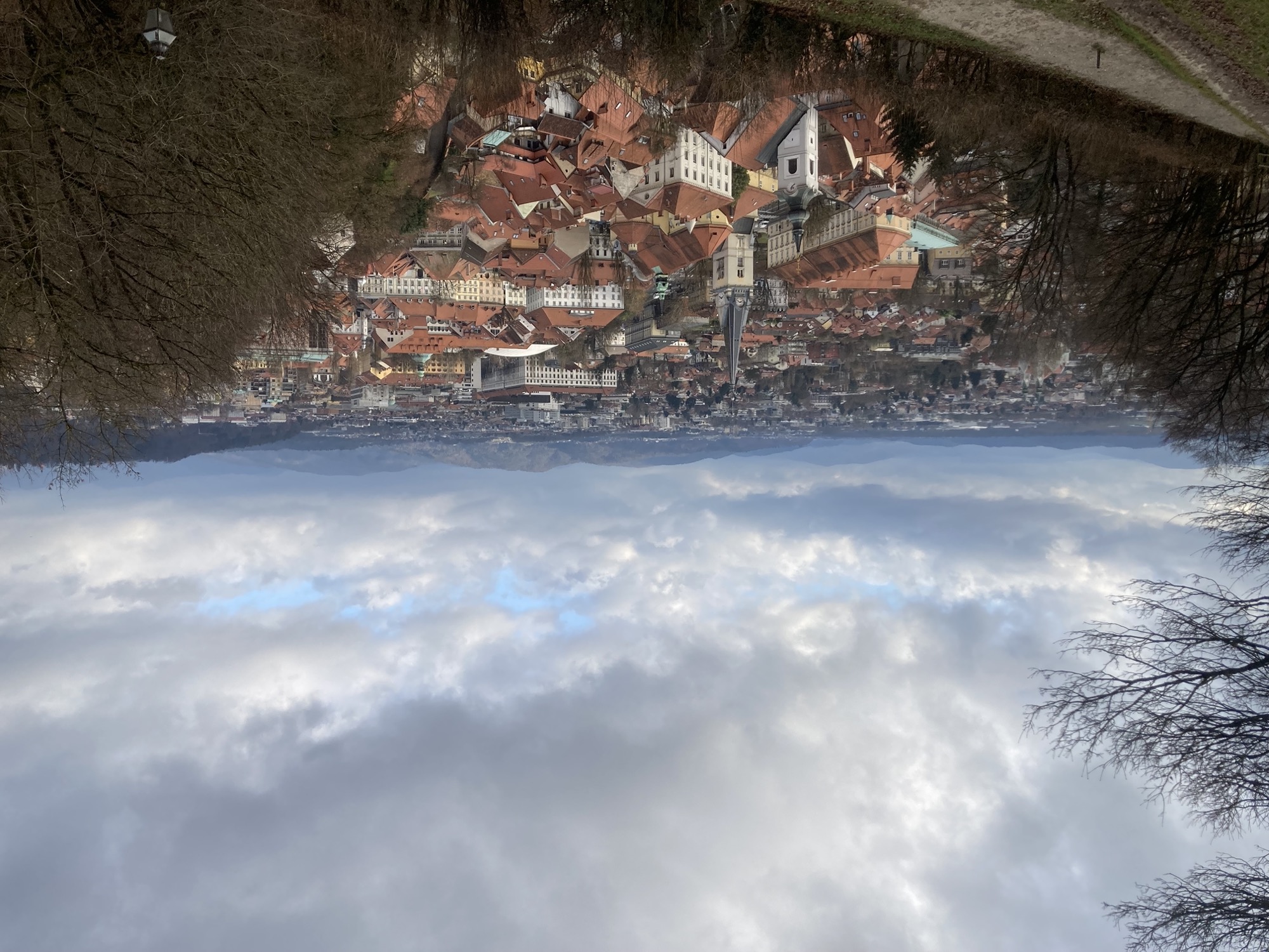 Ausblick vom Schlossberg Richtung Osten, zwei Kirchtürme überragen die Häuser dieses Stadtteils, weiter hinten Hügel und leicht bewölkter Himmel