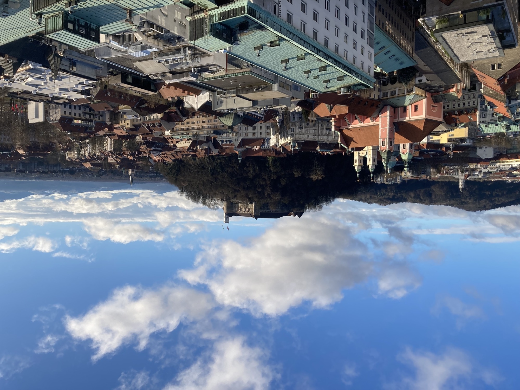 Ausblick von der Dachterrasse eines Wolkenkratzers, links sind die Türme von zwei Kirchen zu sehen, zentral im Bild der Schlossberg mit dem Schloss obendrauf, im Hintergrund Berge und leicht bewölkter Himmel