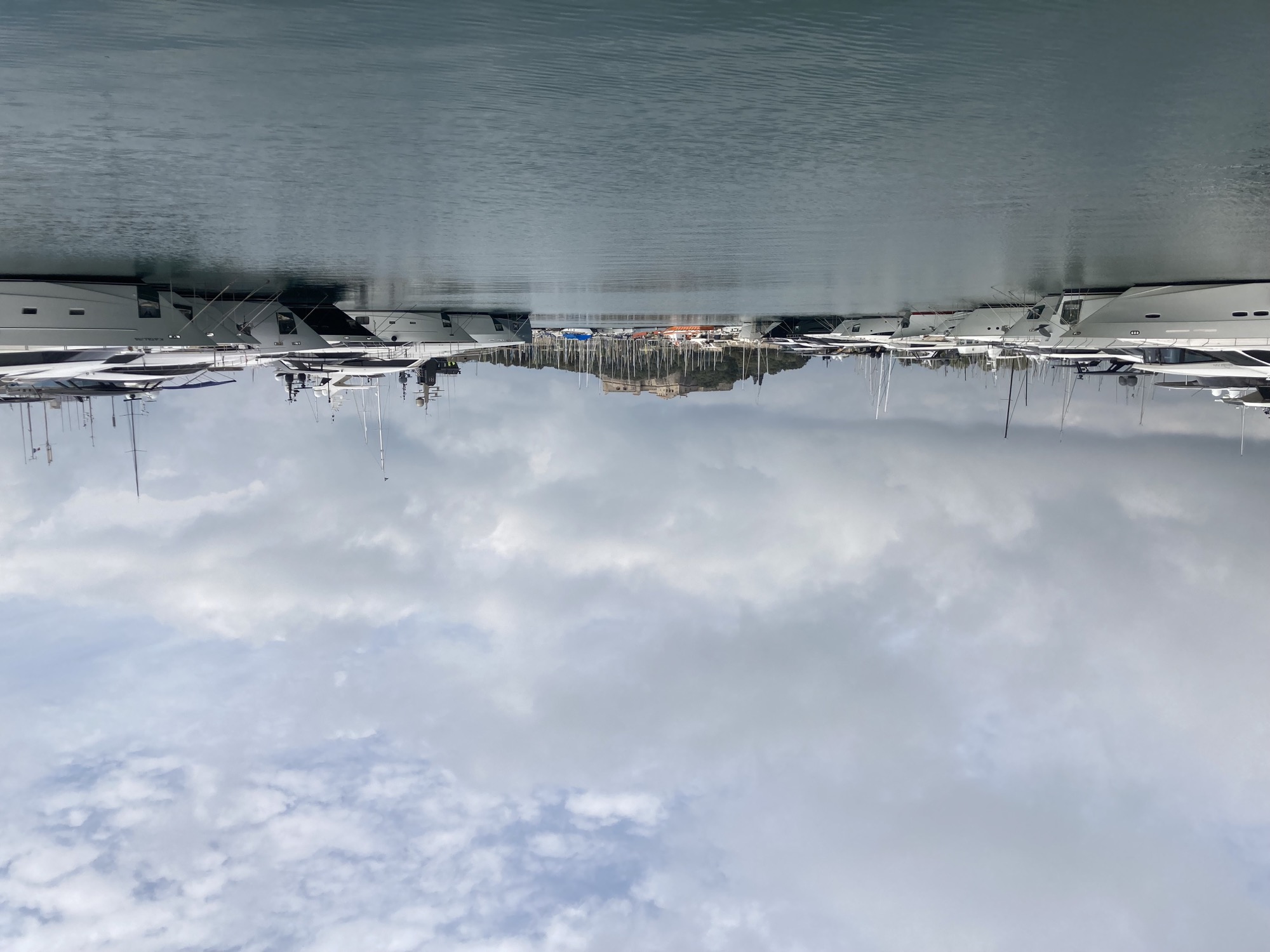 Blick in den Hafen von Antibes, links und rechts große Yachten, in der Mitte Wasser, im Hintergrund der Hügel mit dem zu erahnenden Fort Carré