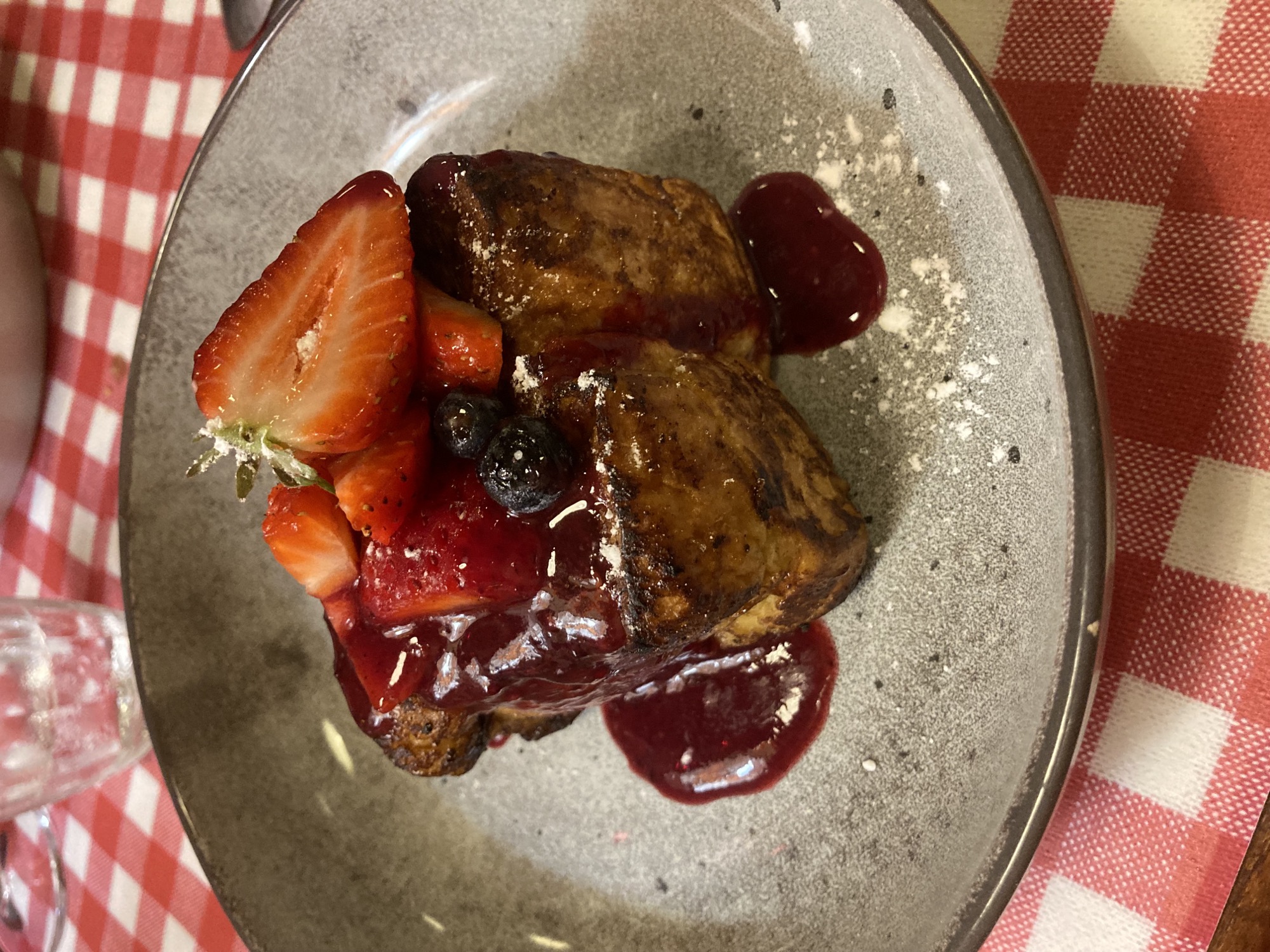 von oben auf den Teller fotografiert, ein Stückchen braun gebranntes Brioche, getoppt mit Erdbeeren und einer dunkelroten Sauce