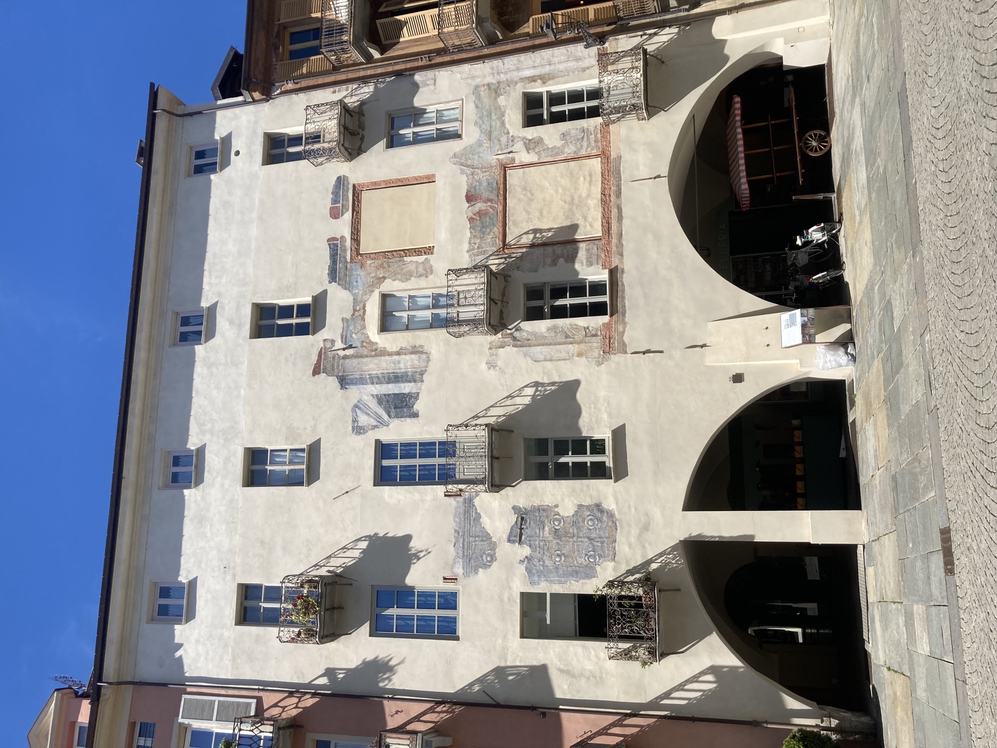Häuserfassade an der zentralen Straße von Cuneo, das Erdgeschoss wird von Rundbögen überspannt und bildet so eine Art Galerie, die im Schatten liegt, die Fassade des Hauses ist teilweise modern neu gestrichen, teilweise zeigt sie Reste von früheren Bemalungen