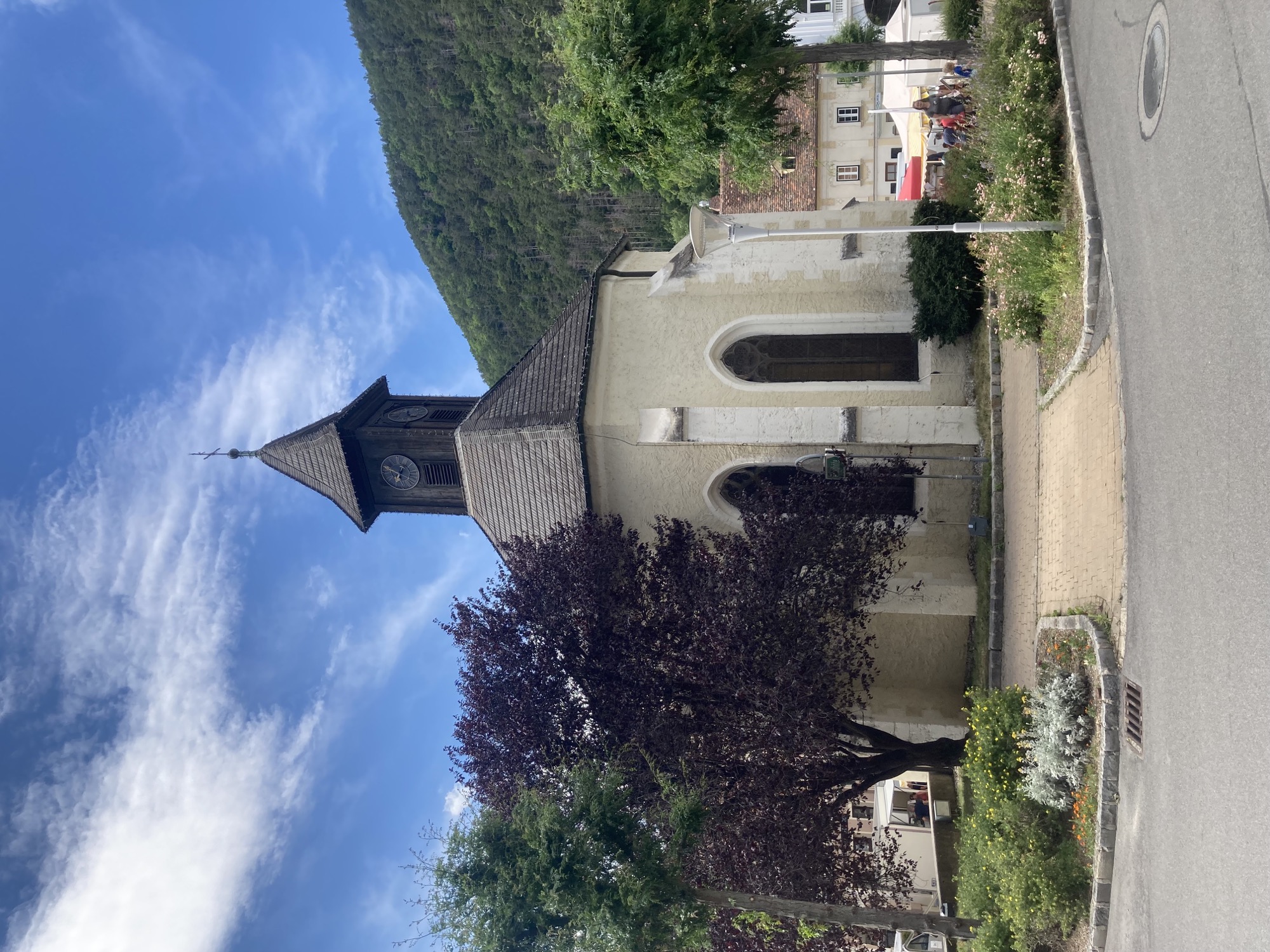 Kapelle mit einem fast runden Grundriss, das Dach besteht aus 8 Teilen in zwei unterschiedlichen Größen, darauf ein niedriger Holzturm mit Uhr und Kreuz