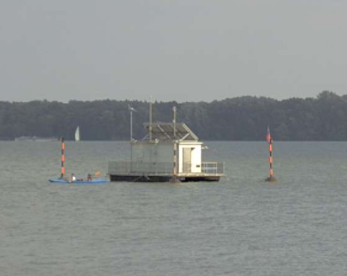 Webcam-Screenshot der Wetterstation, eine Art Floß zwischen zwei orange-schwarz gestreiften Pfeilern, links davor unser blaues Kajak