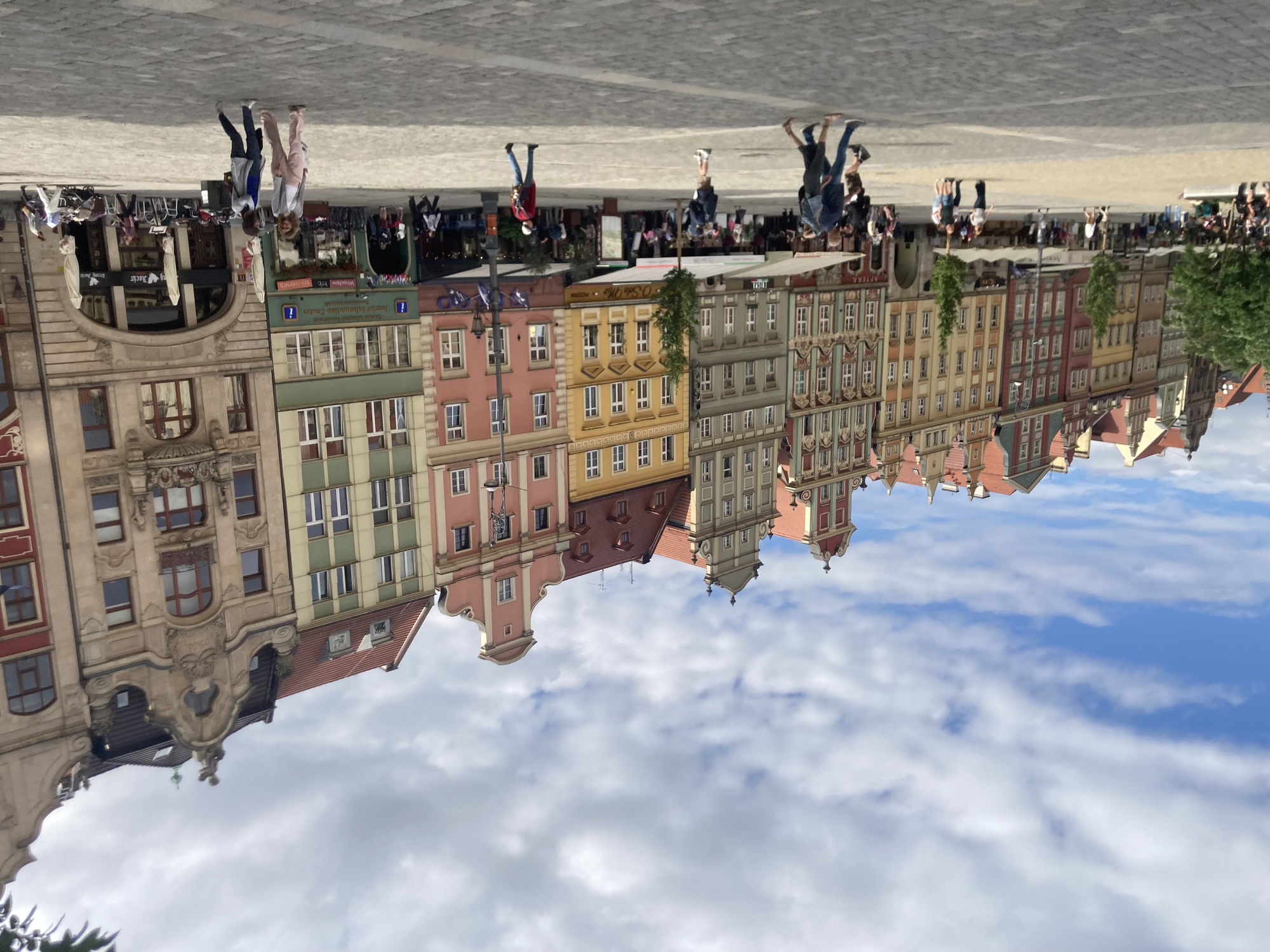 Rathausplatz mit vielen schmalen Häuschen mit Ziergiebeln in verschiedenen pastelligen Farben, davor Gastgärten mit Markiesen darüber, auf dem Platz sind einige Personen unterwegs