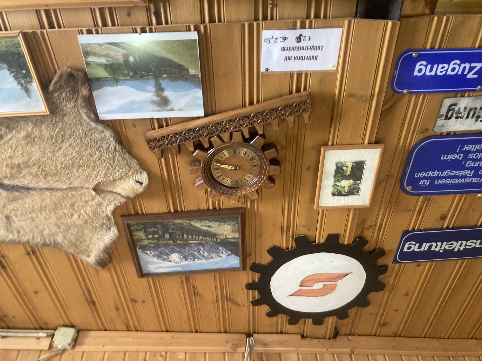holzgetäfelte Wand mit viel Dekoration: ein ÖBB-Logo in einem Zahnrad, mehrere Fotos der Schneebergbahn, eine Uhr in Form eines Zahnrads auf einer Zahnradschiene, blaue ÖBB-Schilder