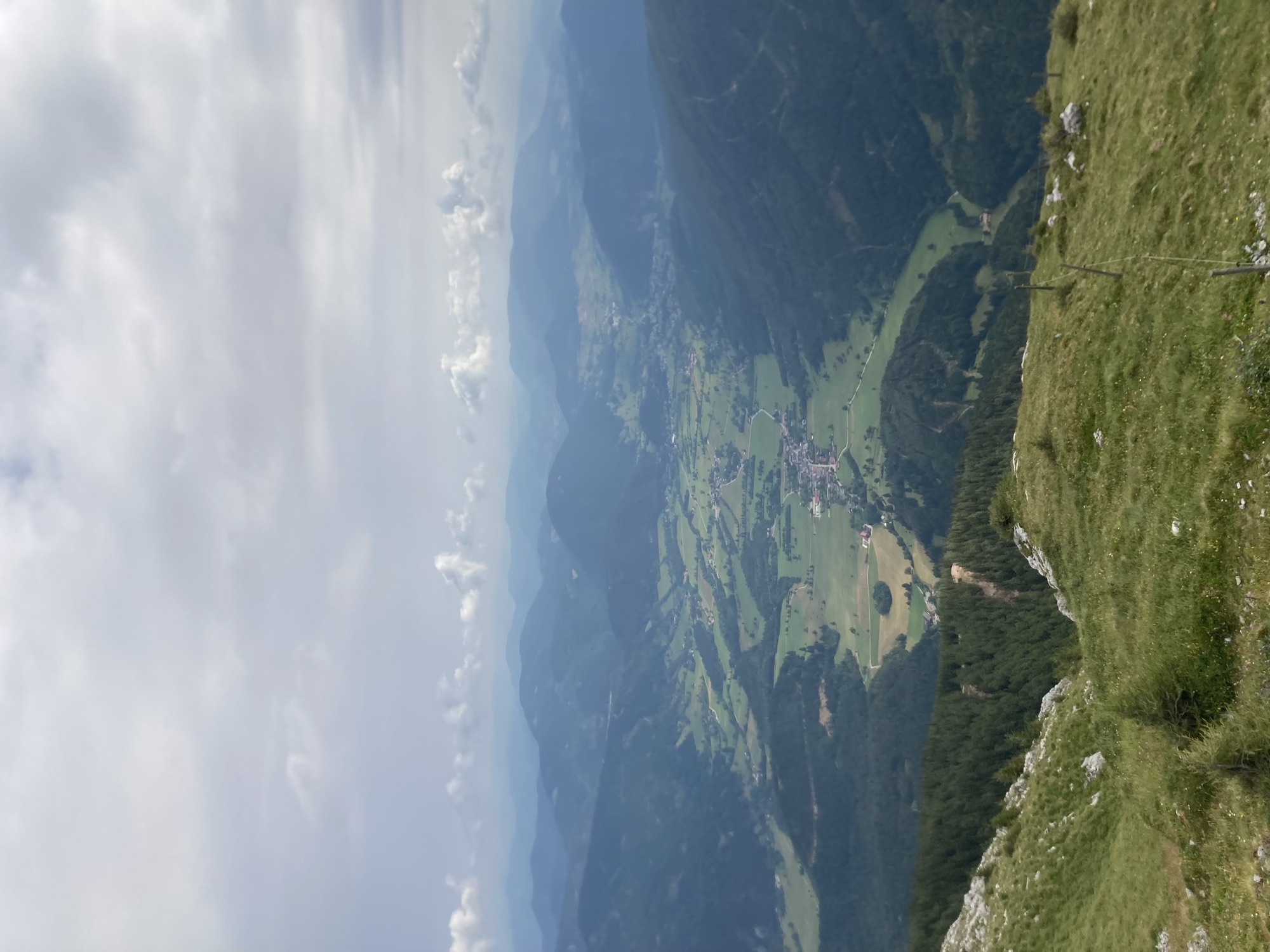 Ausblick ins Tal von der Bergstation der Schneebergbahn, das Tal wird umringt von dunkel bewaldeten Hügeln, im Hintergrund eine Reihe an auffälligen flauschigen Wolken