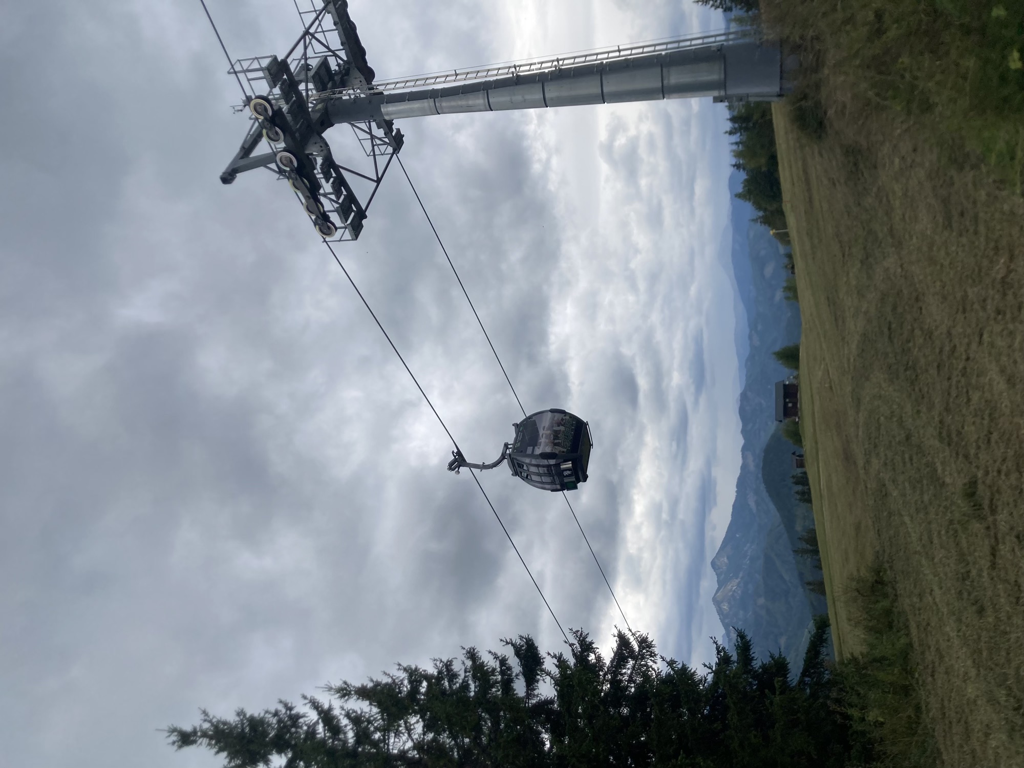 eine Kabine einer Gondelbahn am Seil neben einem Stützpfeiler vor düster bewölktem Himmel